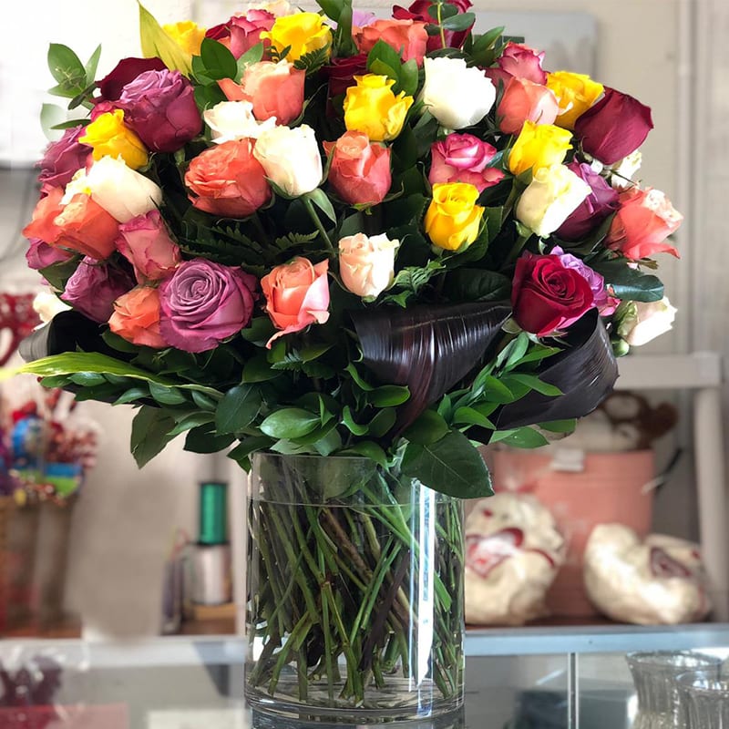 Mixed roses in a clear glass vase with dark ribbon wrap