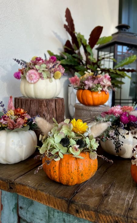 Small white and orange pumpkin arrangements filled with mixed dried flowers on a rustic wooden table