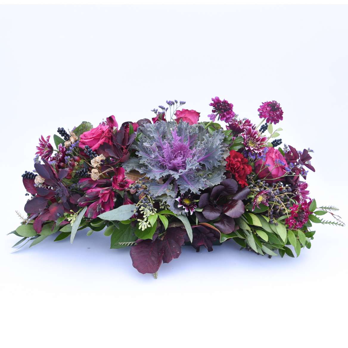 Low centerpiece of purple kale with dark burgundy and pink flowers in an elongated arrangement