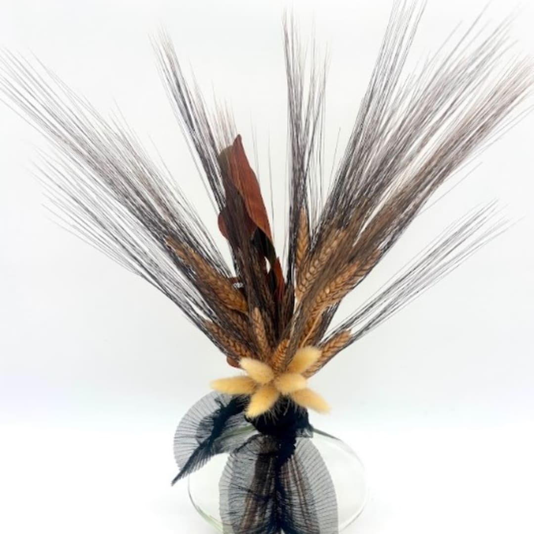 Decorative arrangement of dried grasses and feathers in a clear glass vase