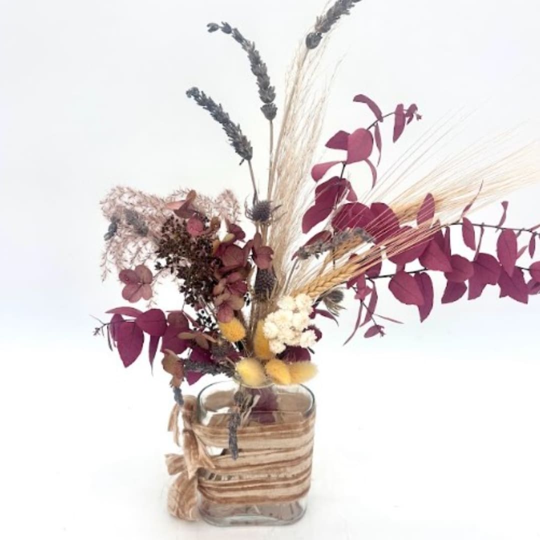 Dried floral arrangement in a clear glass vase with burgundy and beige accents