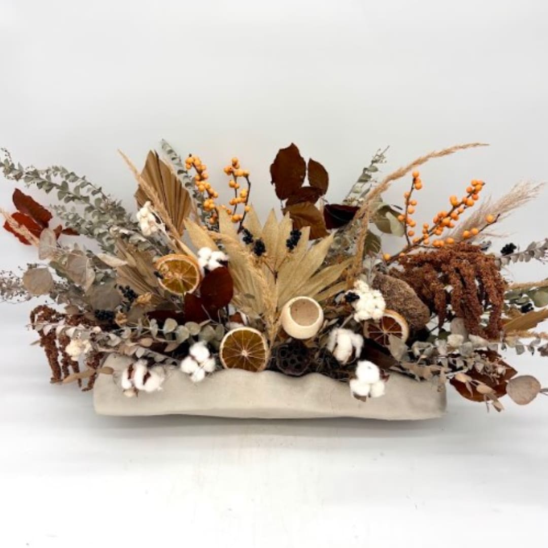 Dried floral arrangement with cotton, orange slices, and seed pods in a low container