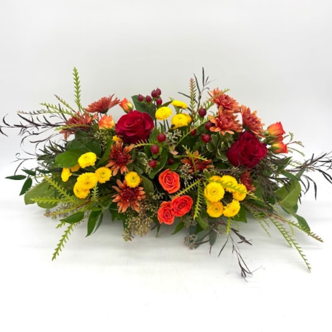 Low floral arrangement with red roses, orange blooms, and yellow pompons