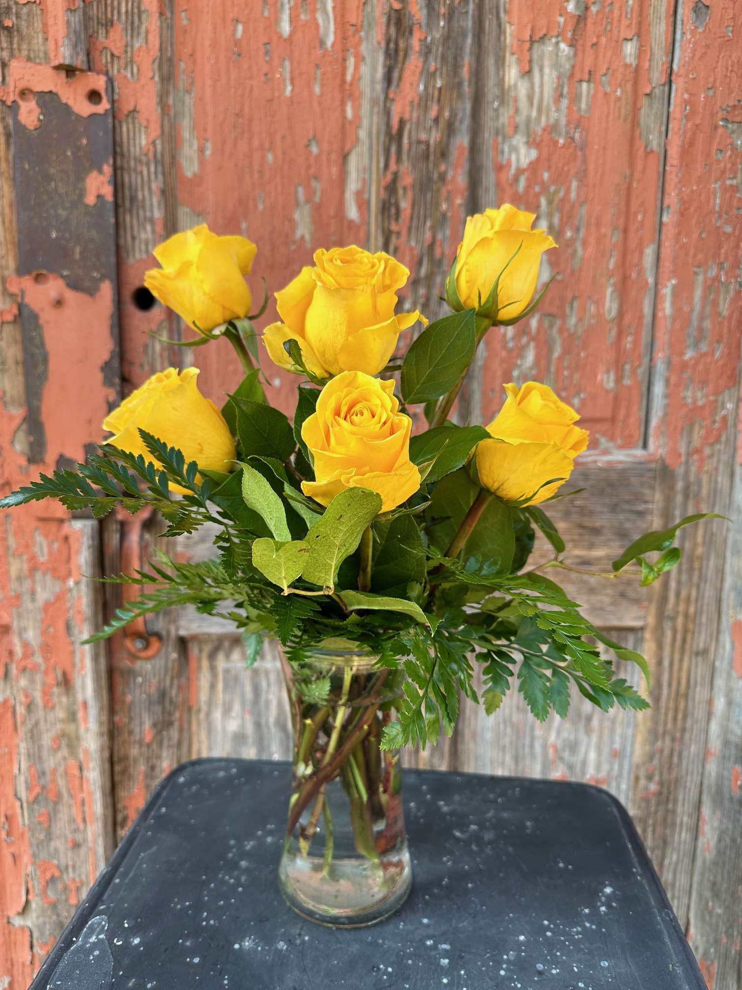 Yellow roses in a clear glass vase with greenery