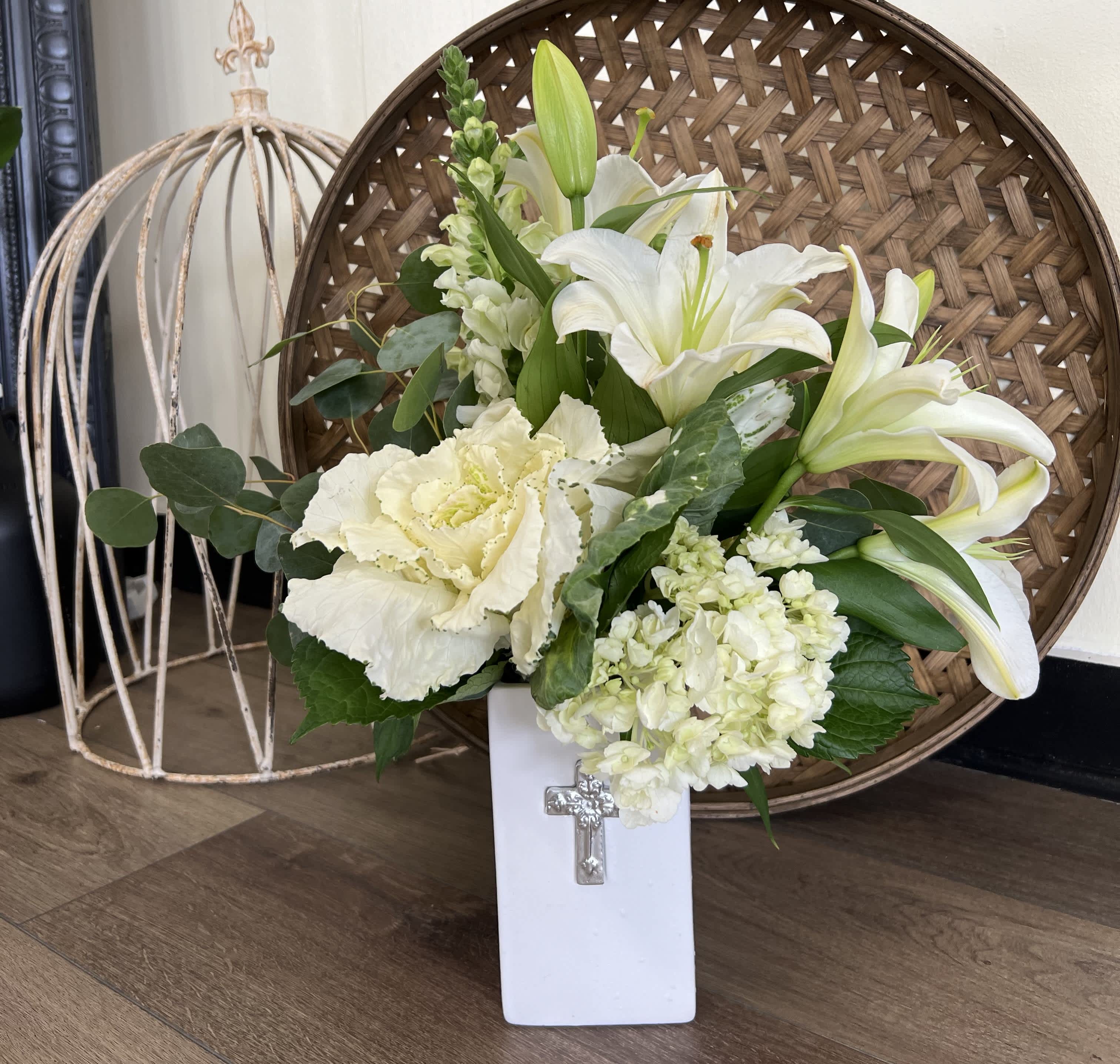 White lilies and pale flowers in a white vase with a cross emblem