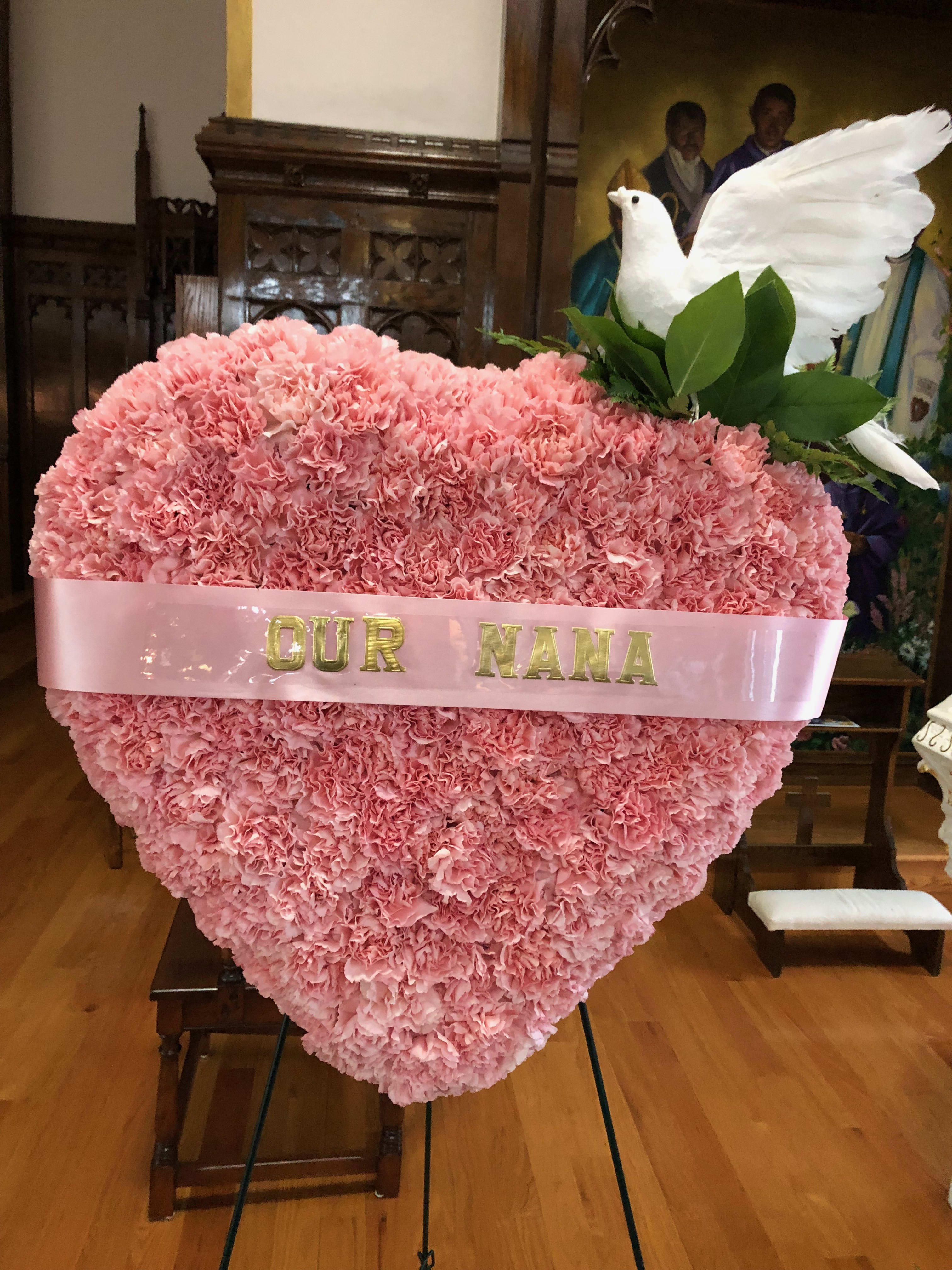 Pink carnation heart arrangement with a white dove topper and ribbon