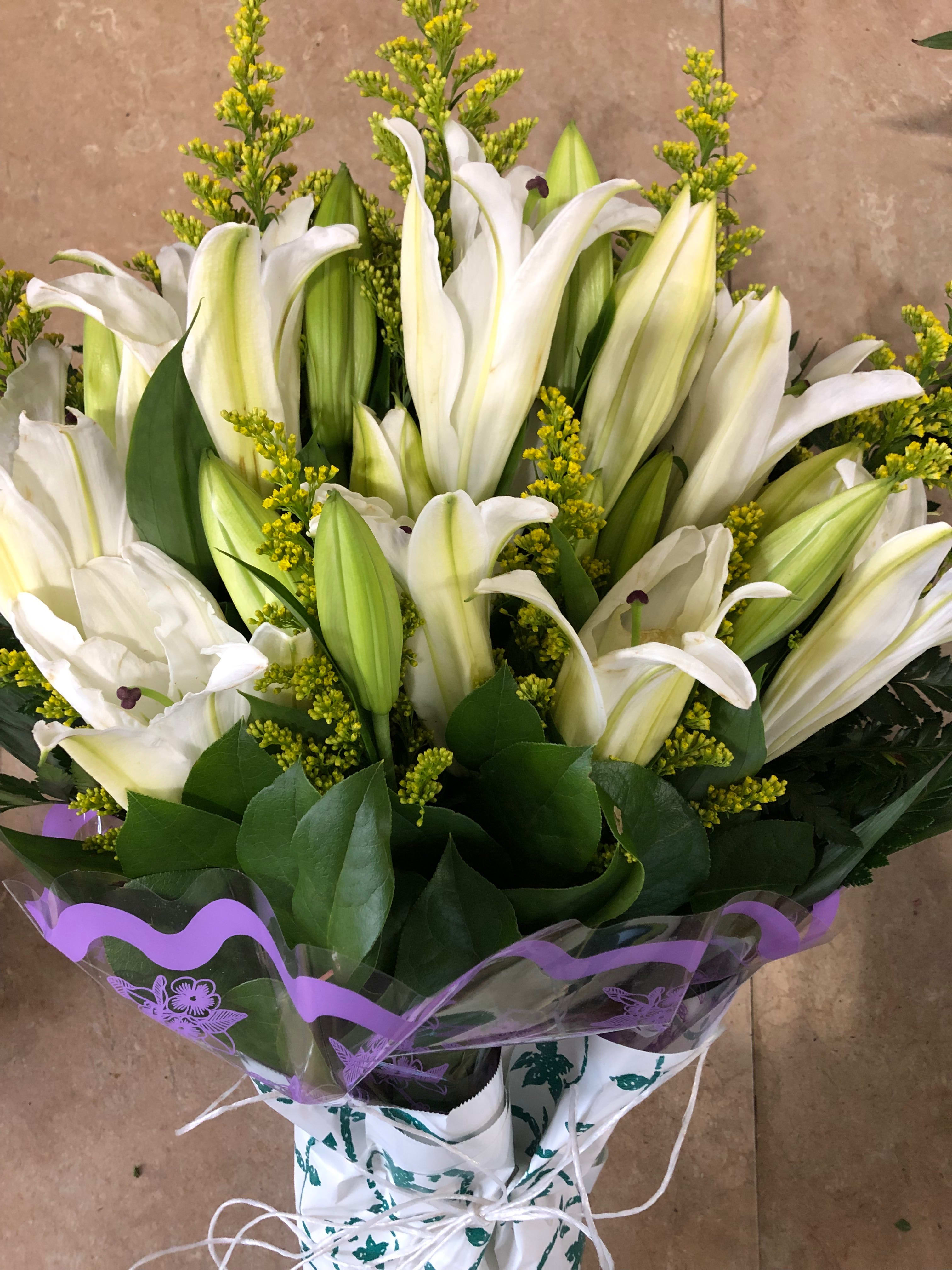 Bouquet of white lilies with yellow filler flowers and purple wrap
