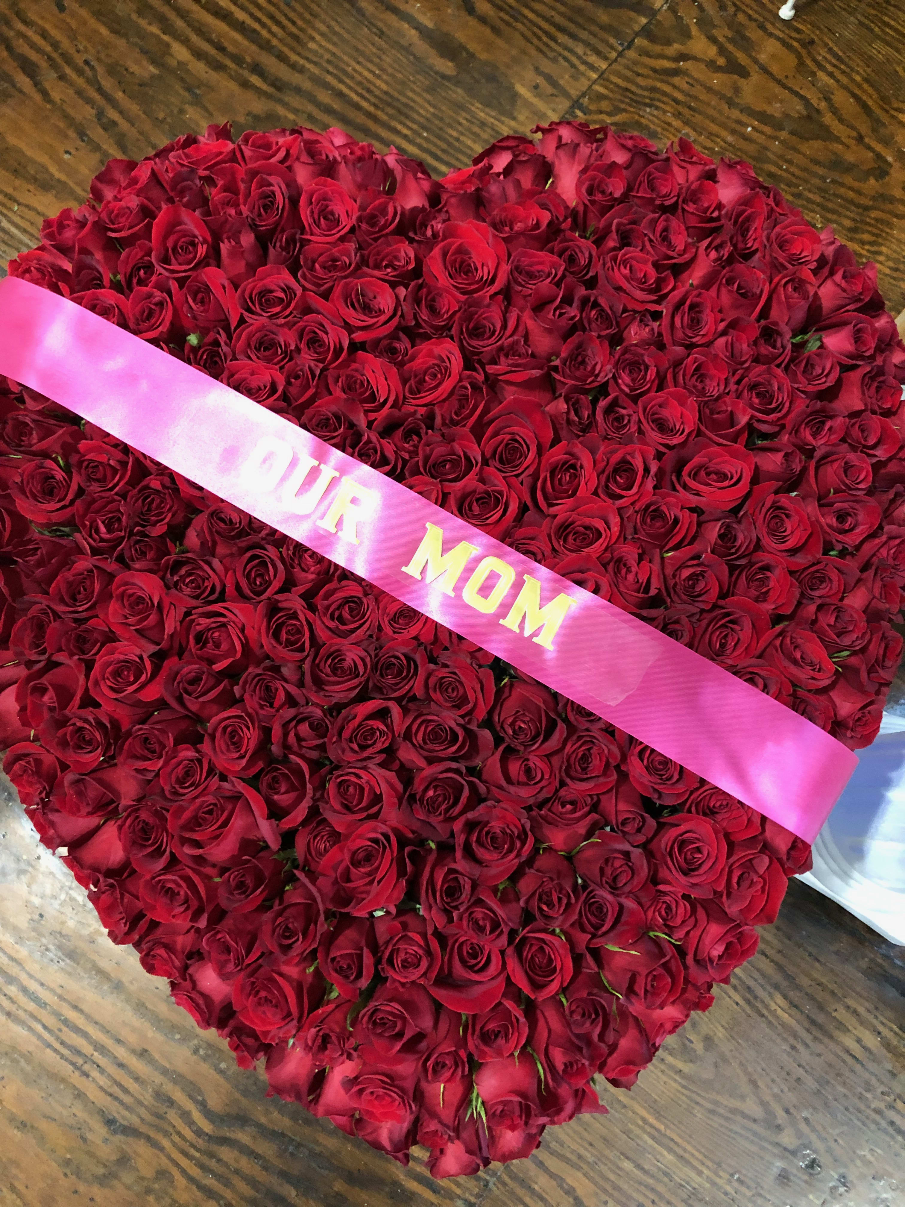 Heart-shaped bouquet of red roses with a pink ribbon