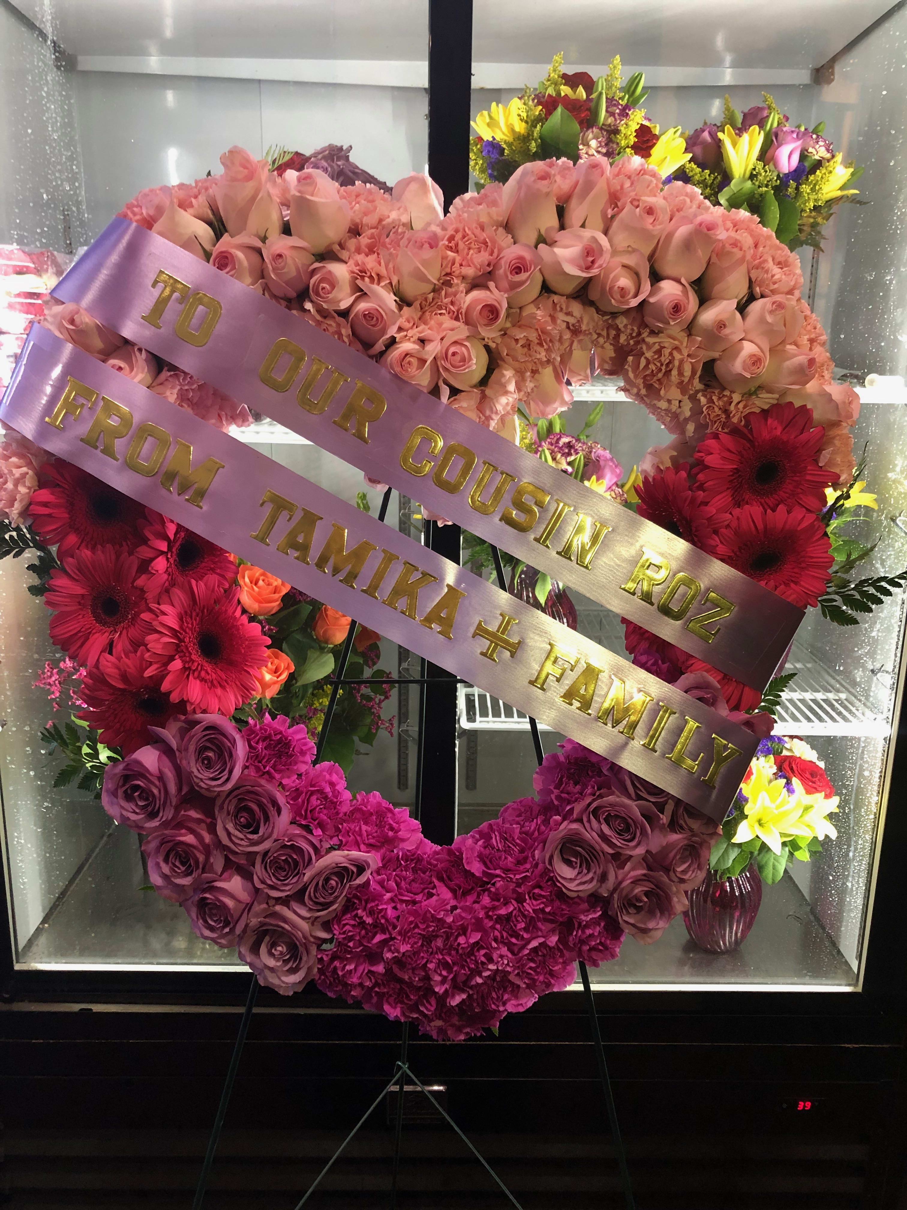 Heart-shaped floral wreath with pink roses and gerberas, with ribbon text