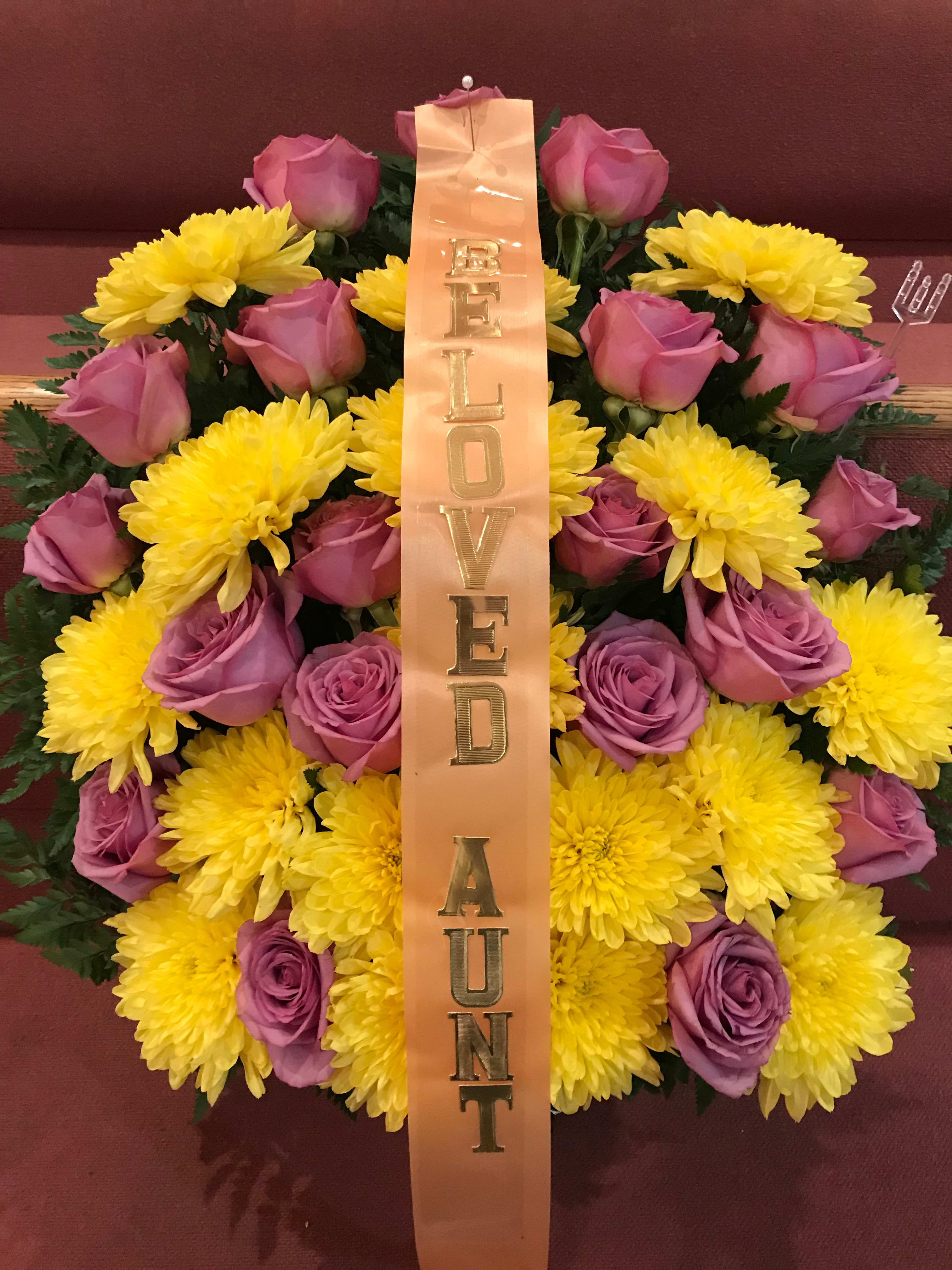 Pink roses and yellow chrysanthemums with a vertical ribbon reading "BELOVED AUNT"