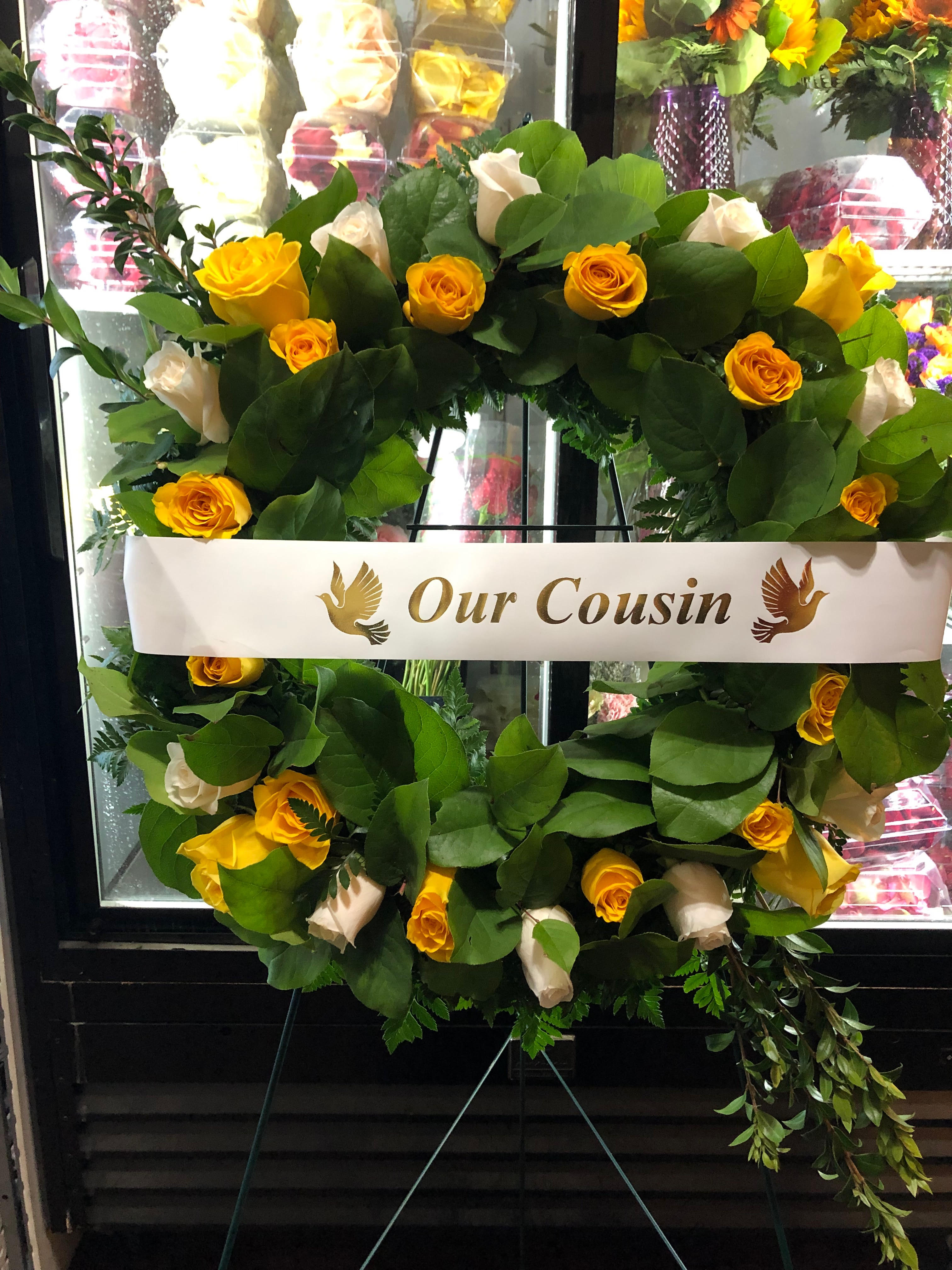 Yellow and white rose wreath on an easel with a memorial ribbon