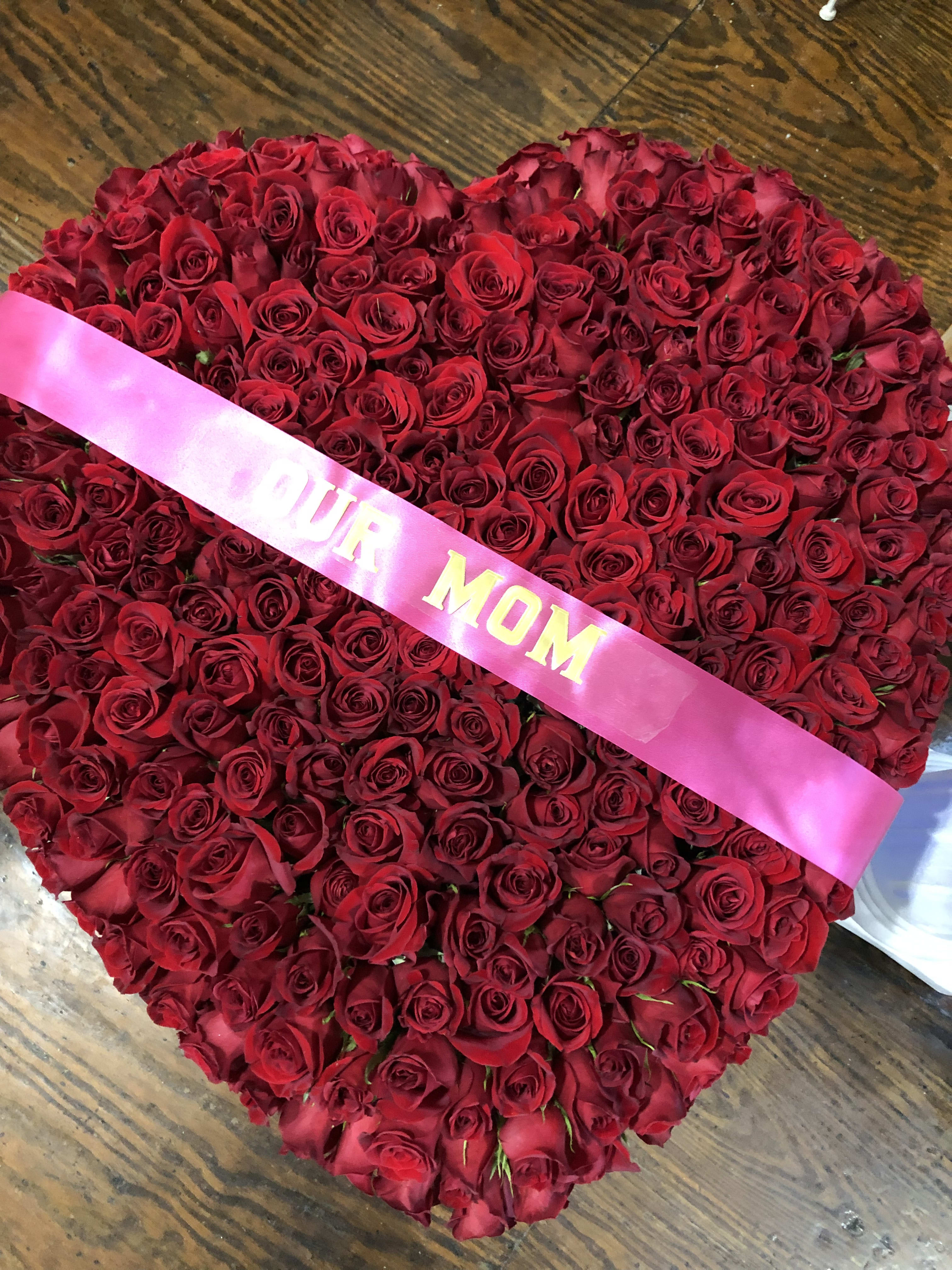 Heart-shaped bouquet of red roses with a pink ribbon
