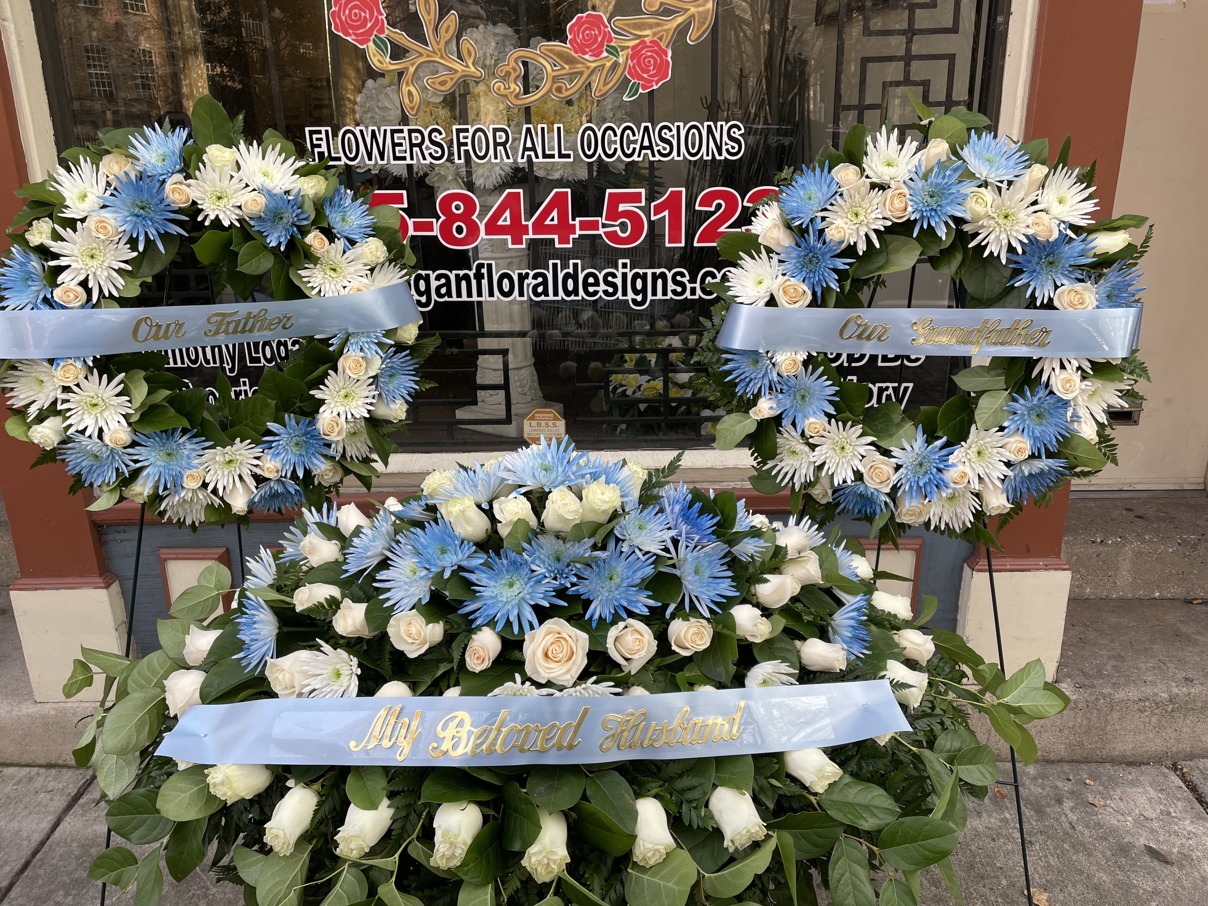 Three blue and white floral wreaths with memorial ribbons