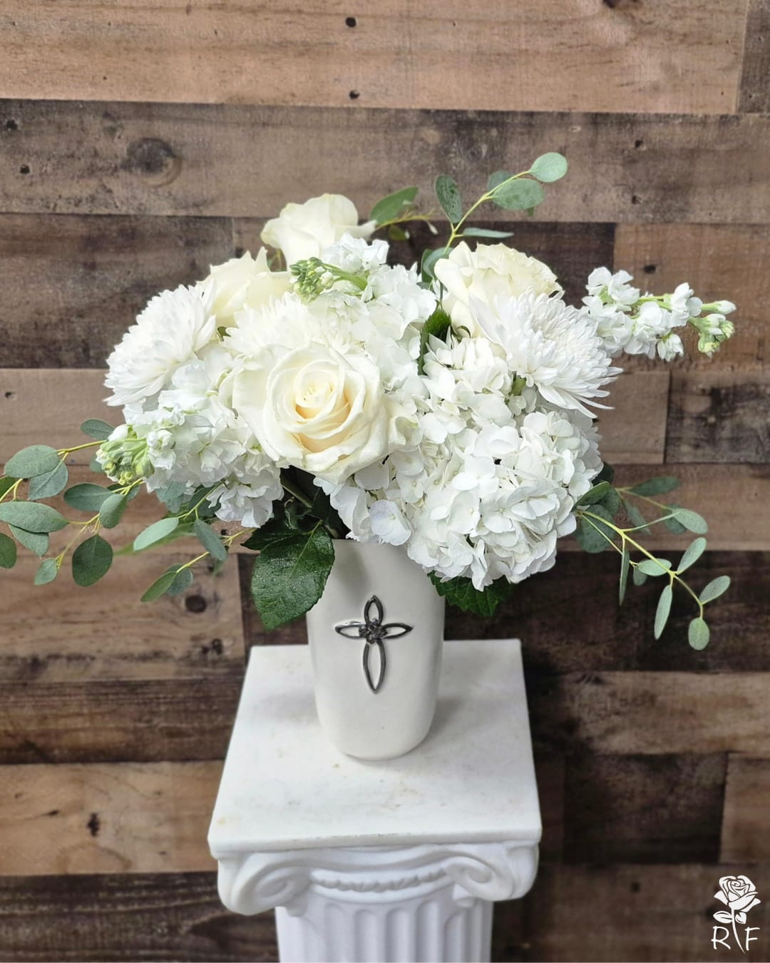 Eternal Peace - The Eternal Peace Bouquet: A profound tribute to a life well-lived, this arrangement brings together the purest white blooms to offer comfort and hope. Featuring crisp white roses, delicate hydrangeas, and classic chrysanthemums, the "Eternal Peace" is accented with airy eucalyptus for a soft, natural touch. Presented in a keepsake ceramic vase adorned with a silver-toned cross, it serves as a lasting symbol of faith and remembrance.