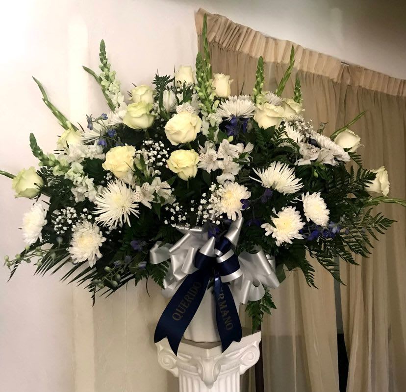 Large white floral arrangement in a pedestal vase with a ribbon bow