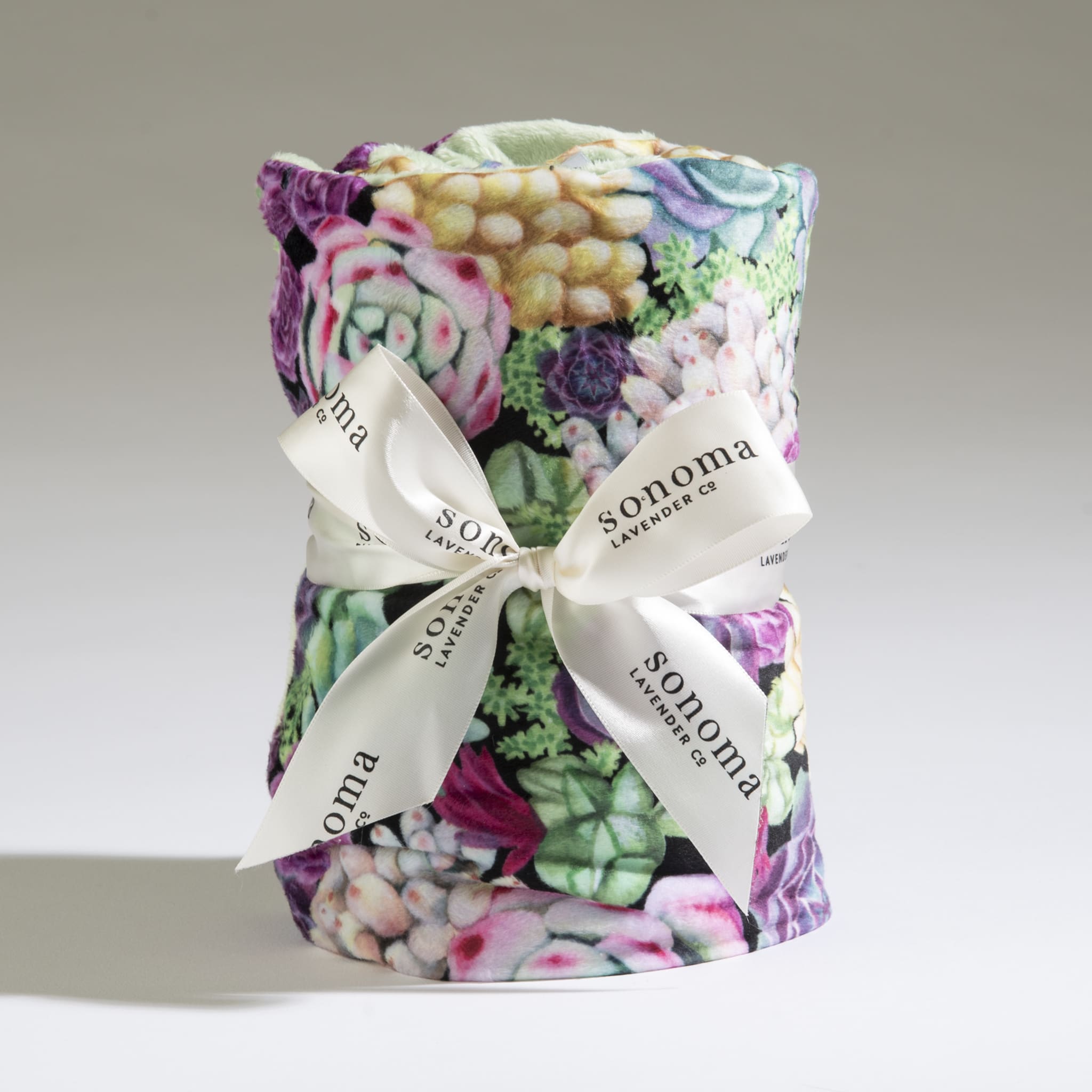 Rolled plush blanket with colorful succulent print tied with a white logo ribbon