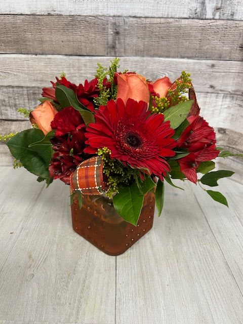 Red and peach flower arrangement in a brown vase with ribbon