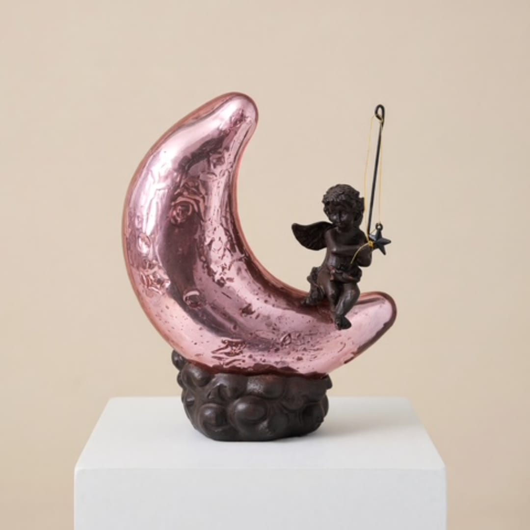 Pink crescent moon sculpture with a small cherub figure on a pedestal