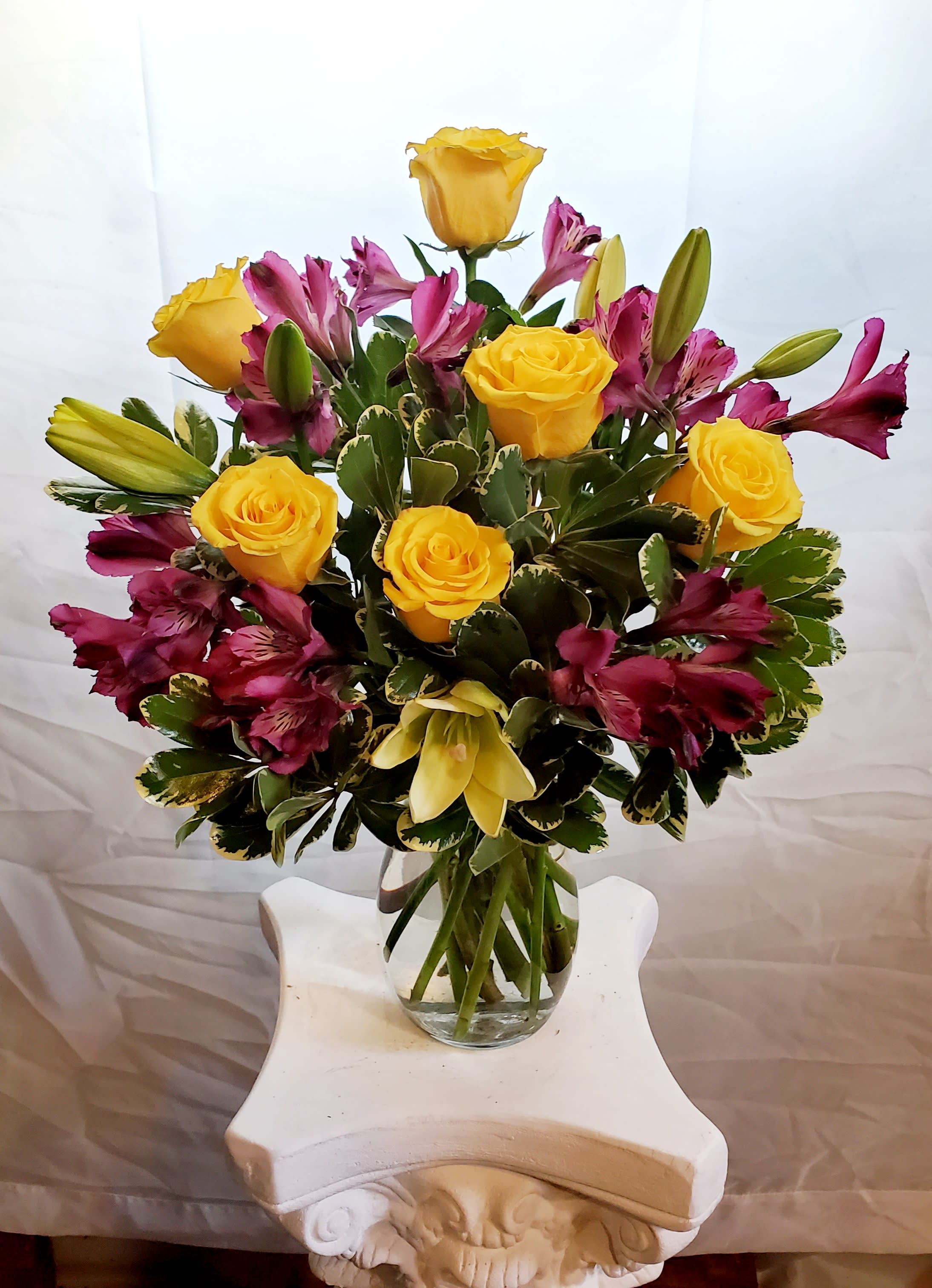 Yellow roses and magenta lilies arranged in a glass vase