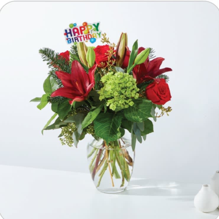 Red lilies and roses in a glass vase with a Happy Birthday pick
