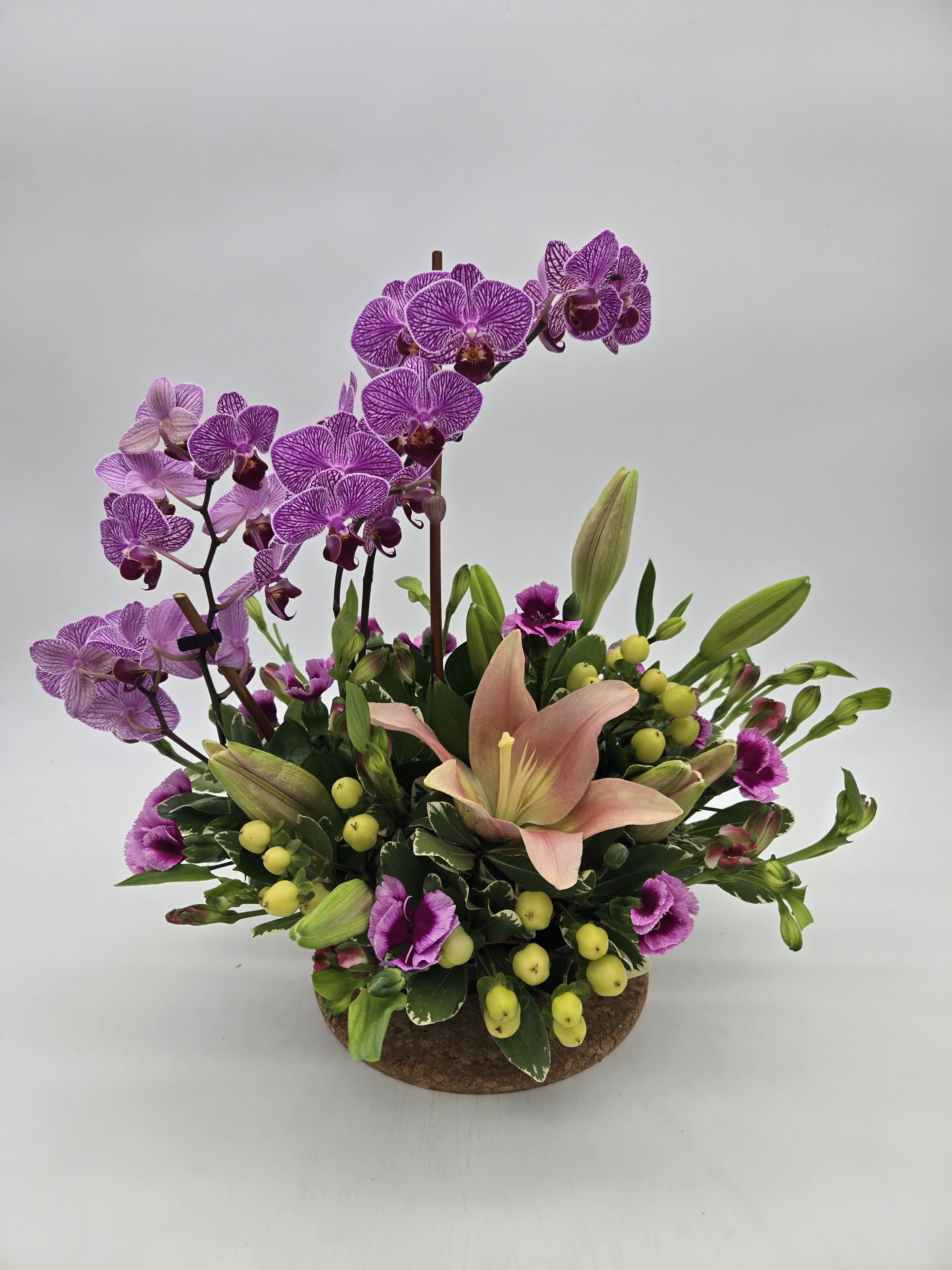 Purple orchids and a peach lily arranged in a low round container