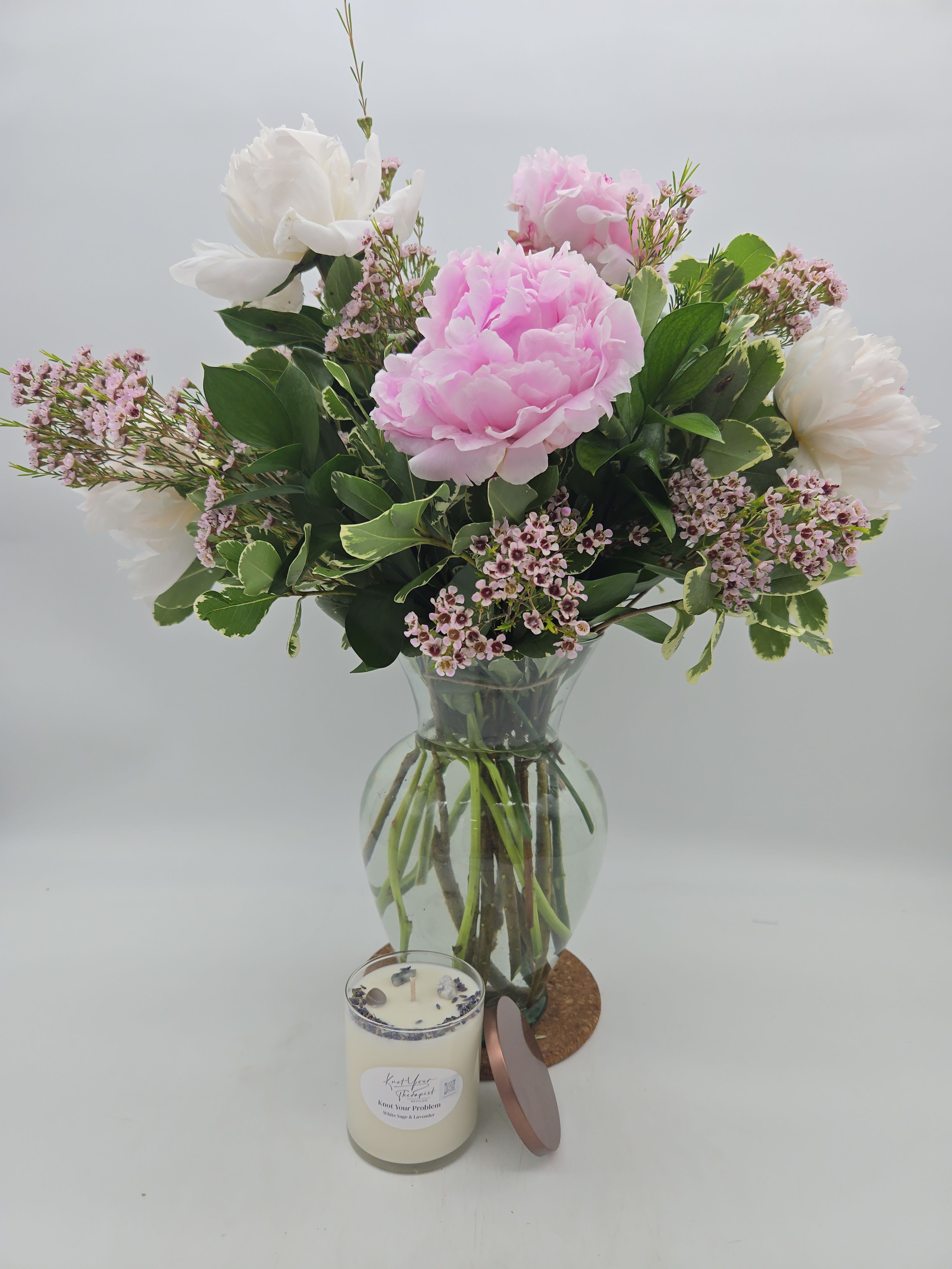 Pink and white flowers in a glass vase with a candle in front