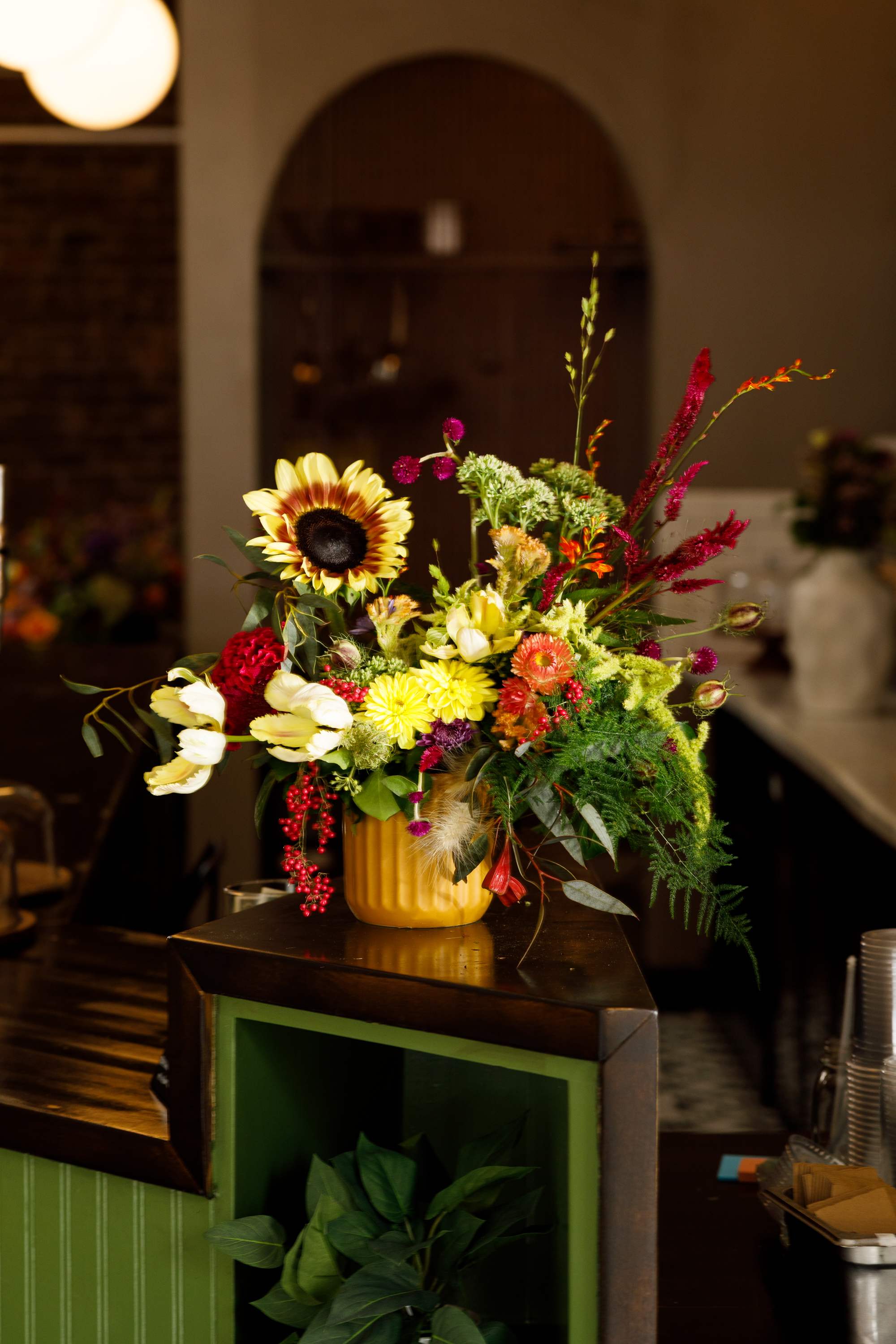 Colorful mixed flower arrangement in a yellow vase on a counter