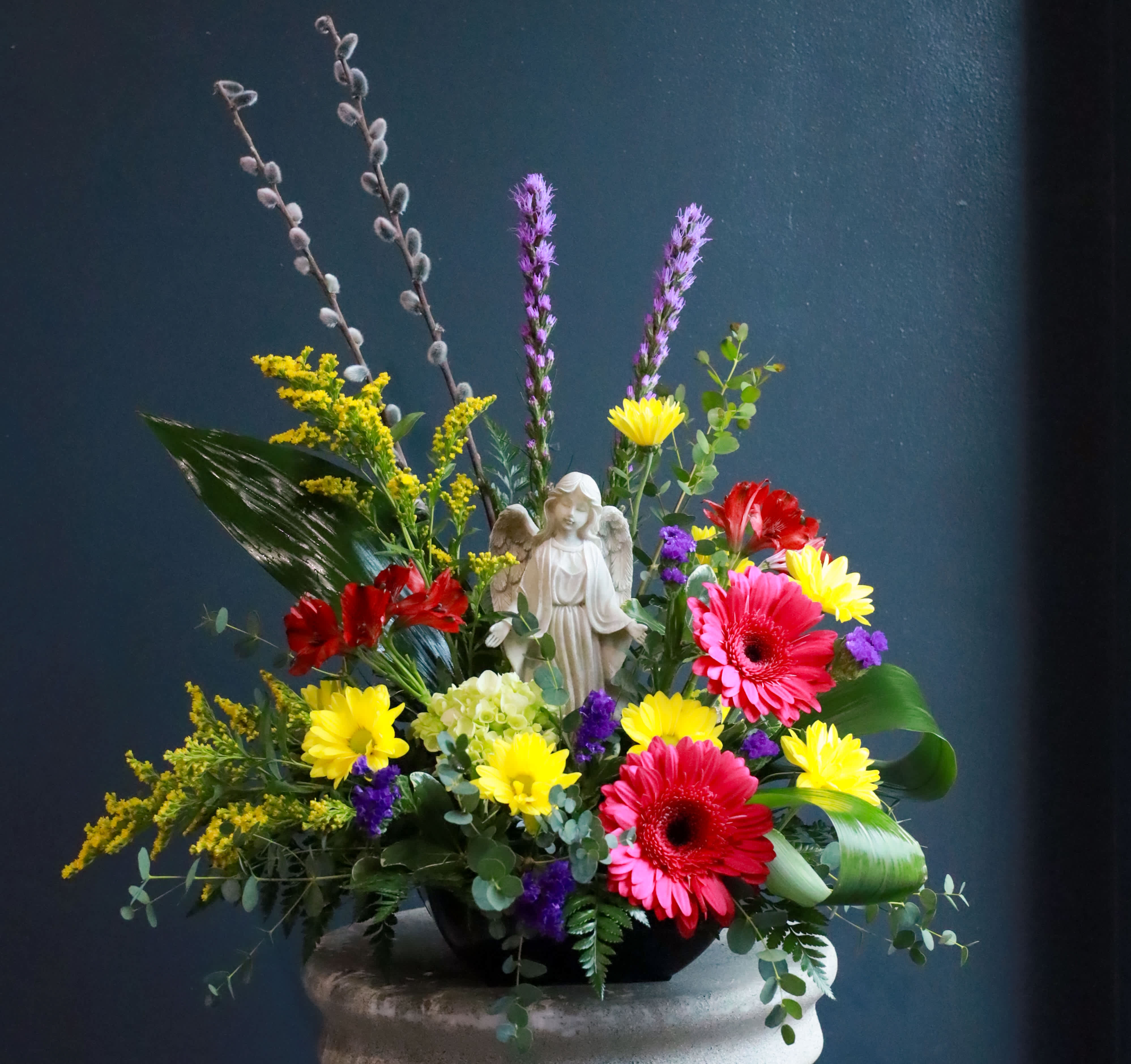 Colorful floral arrangement with an angel figurine in a low black bowl