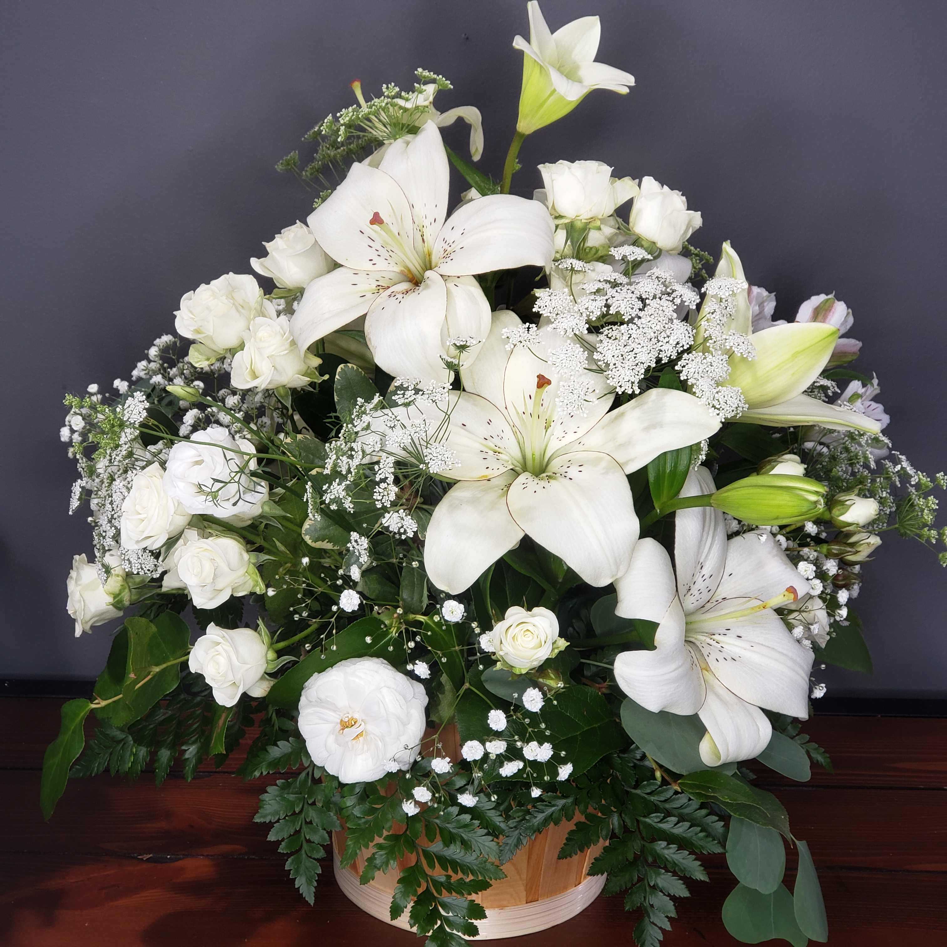 White lilies and roses arranged in a round basket