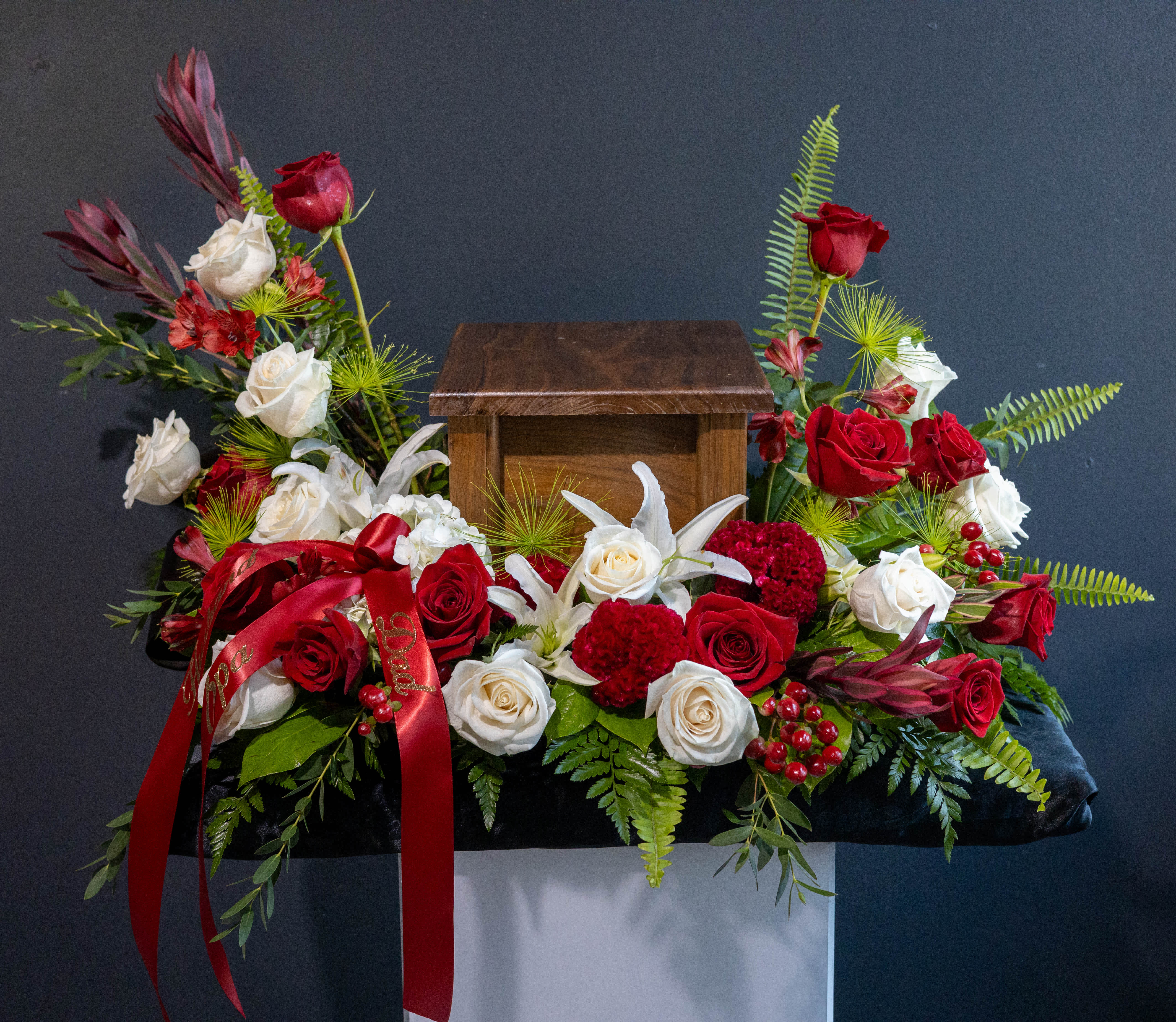 Red and white roses arranged around a wooden urn with a red ribbon