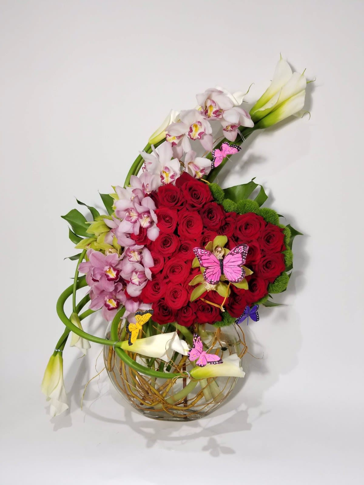 Red roses and pink orchids in a glass vase with butterfly picks