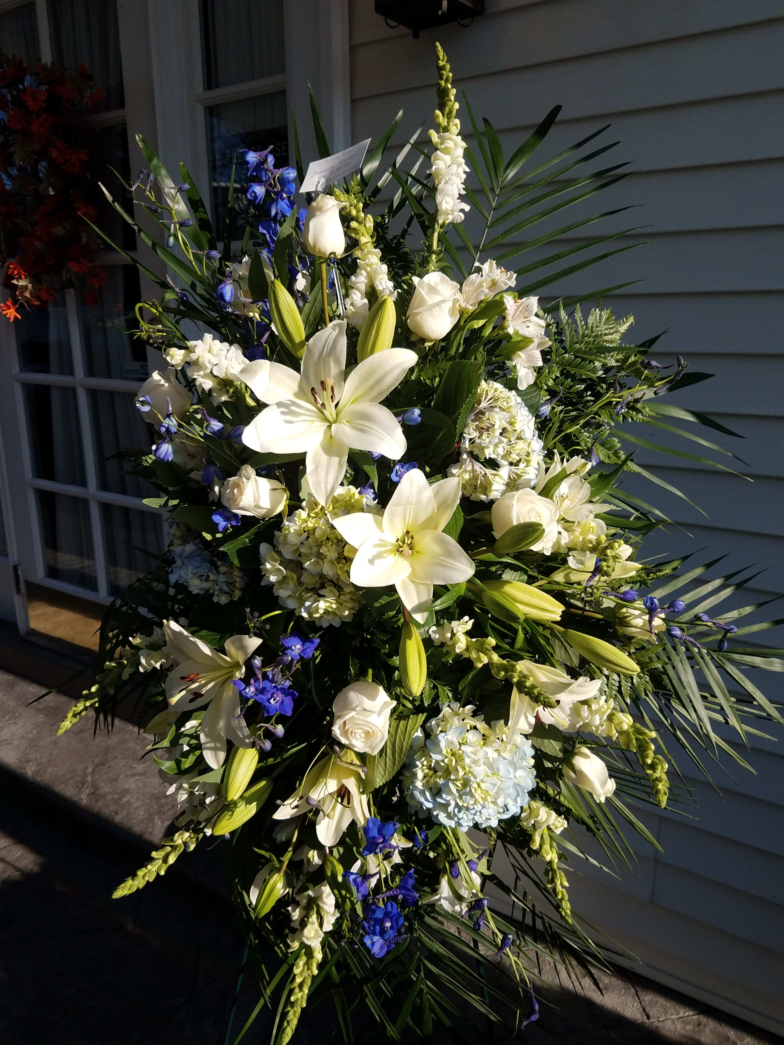 Tall white floral spray with lilies, roses, and blue accents