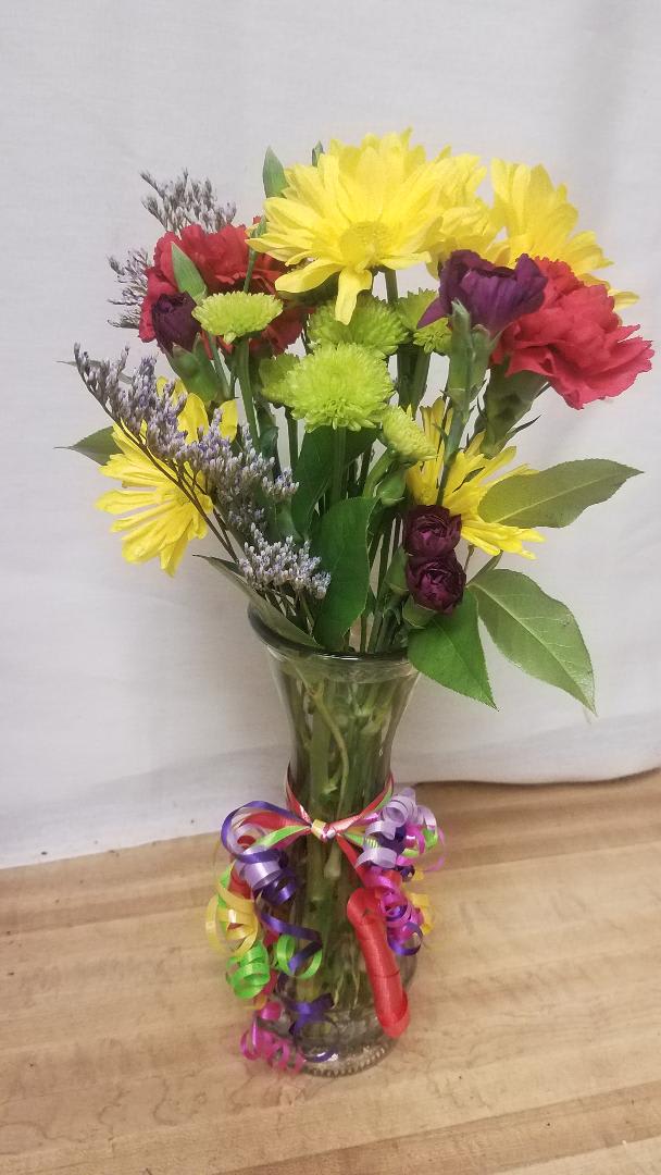 Mixed bouquet of yellow, red, and purple flowers in a clear glass vase