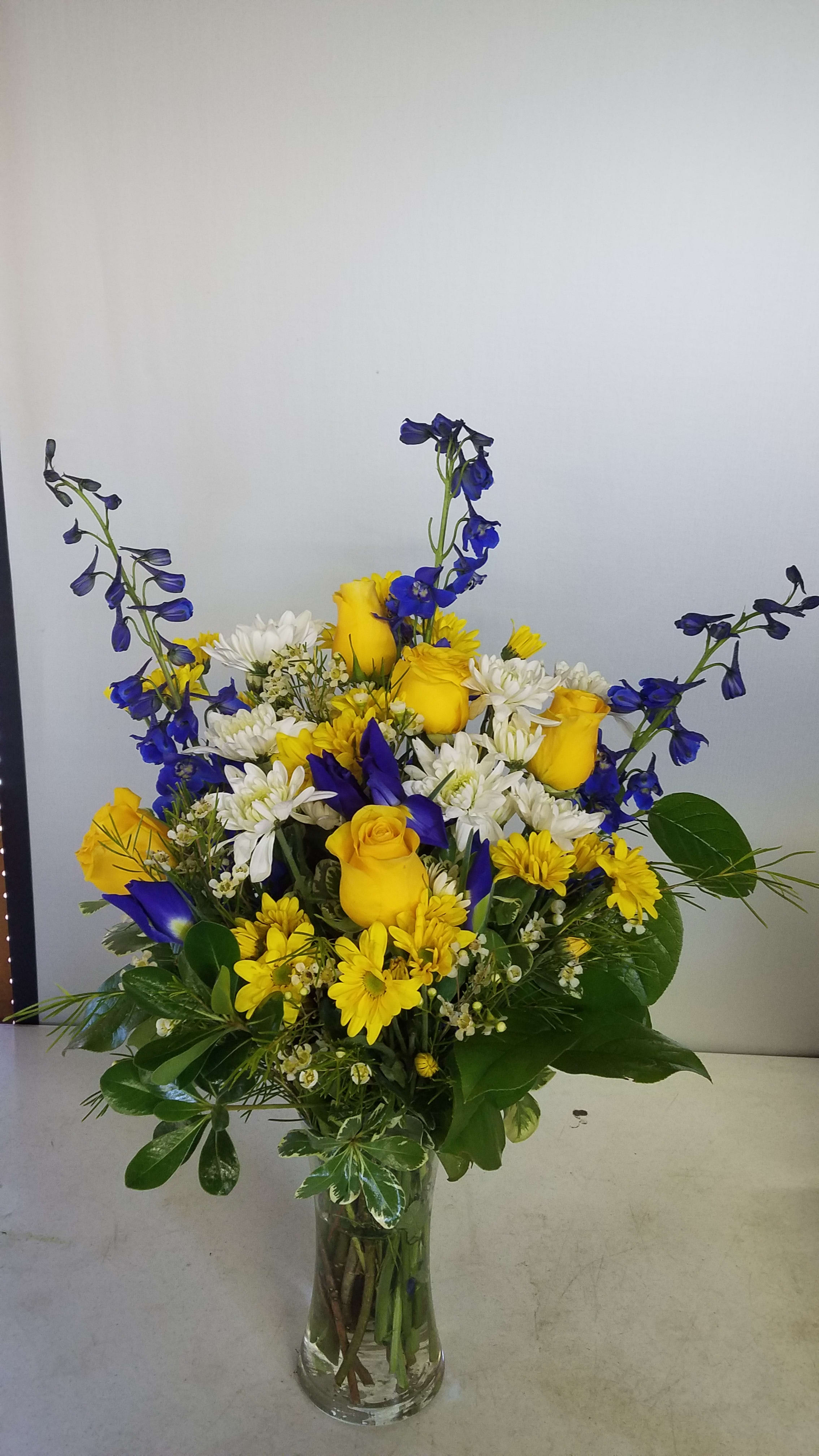 Yellow roses and white daisies in a clear glass vase with blue flowers