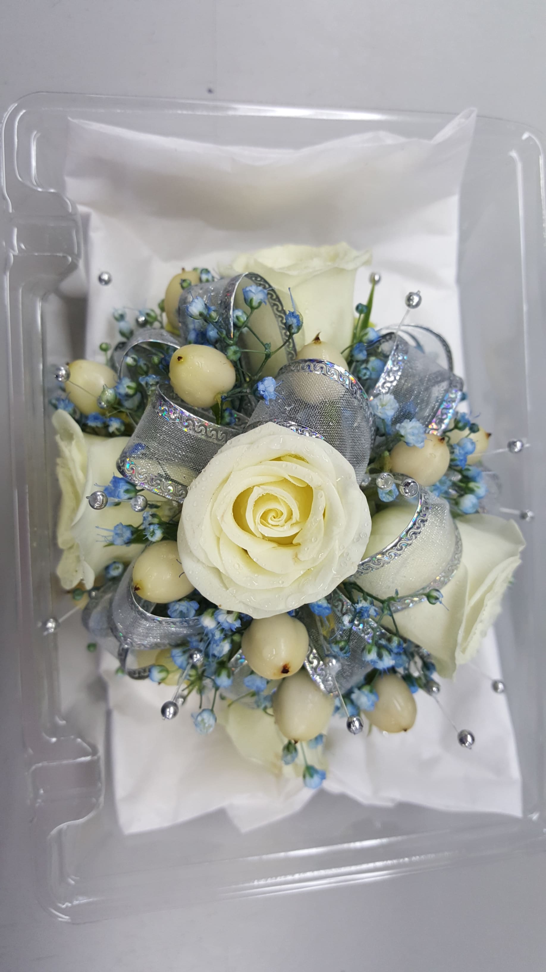 White rose bouquet with blue accents and silver ribbon in a clear box