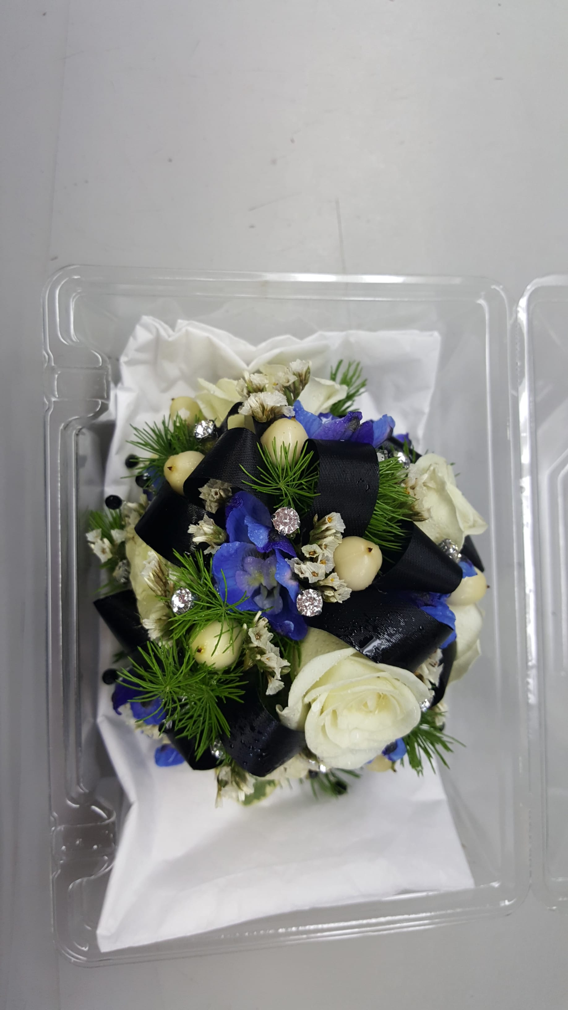 Small bouquet with white and blue flowers in a clear plastic box