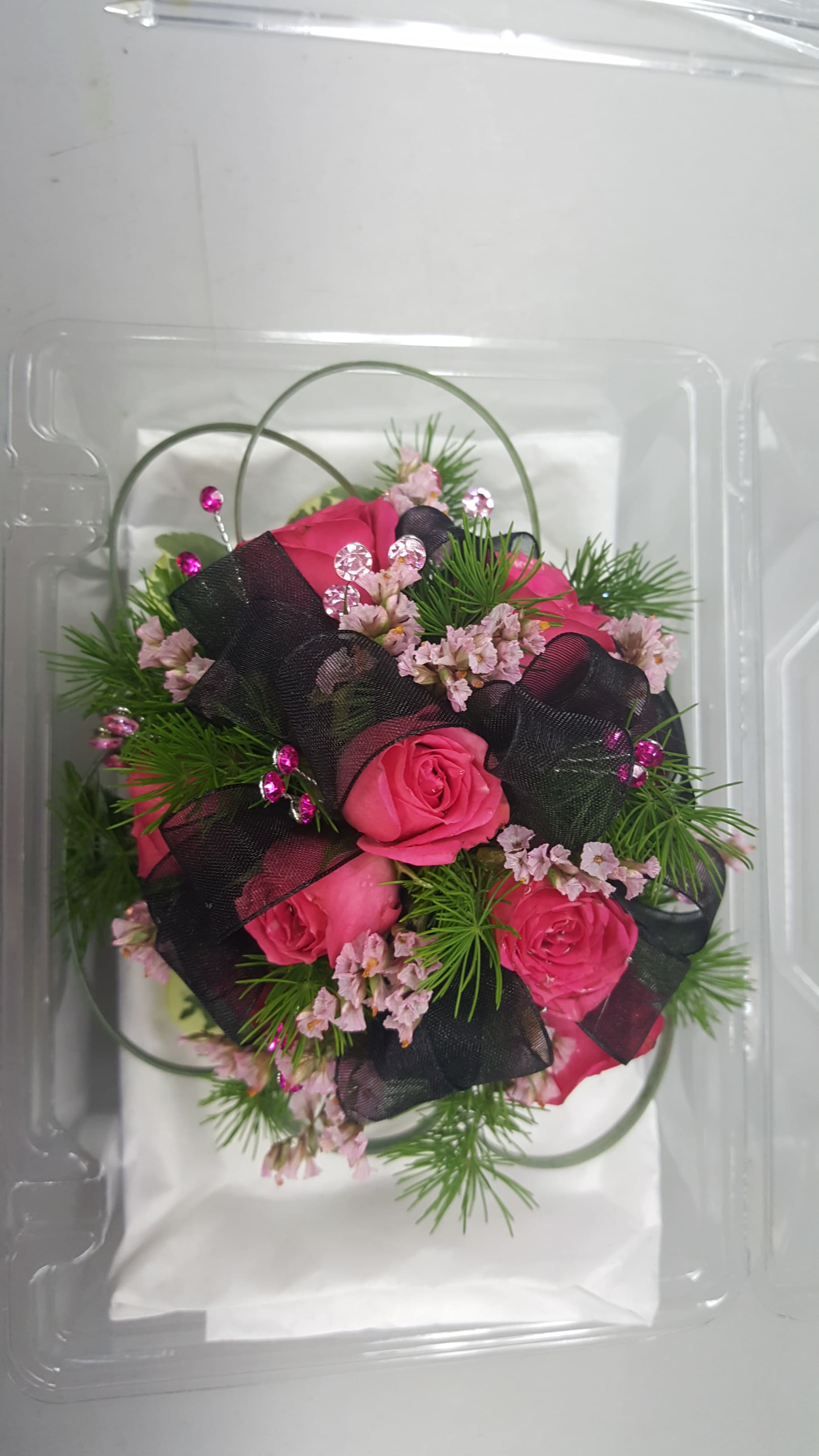 Pink roses with black ribbon and decorative greenery in a clear plastic box