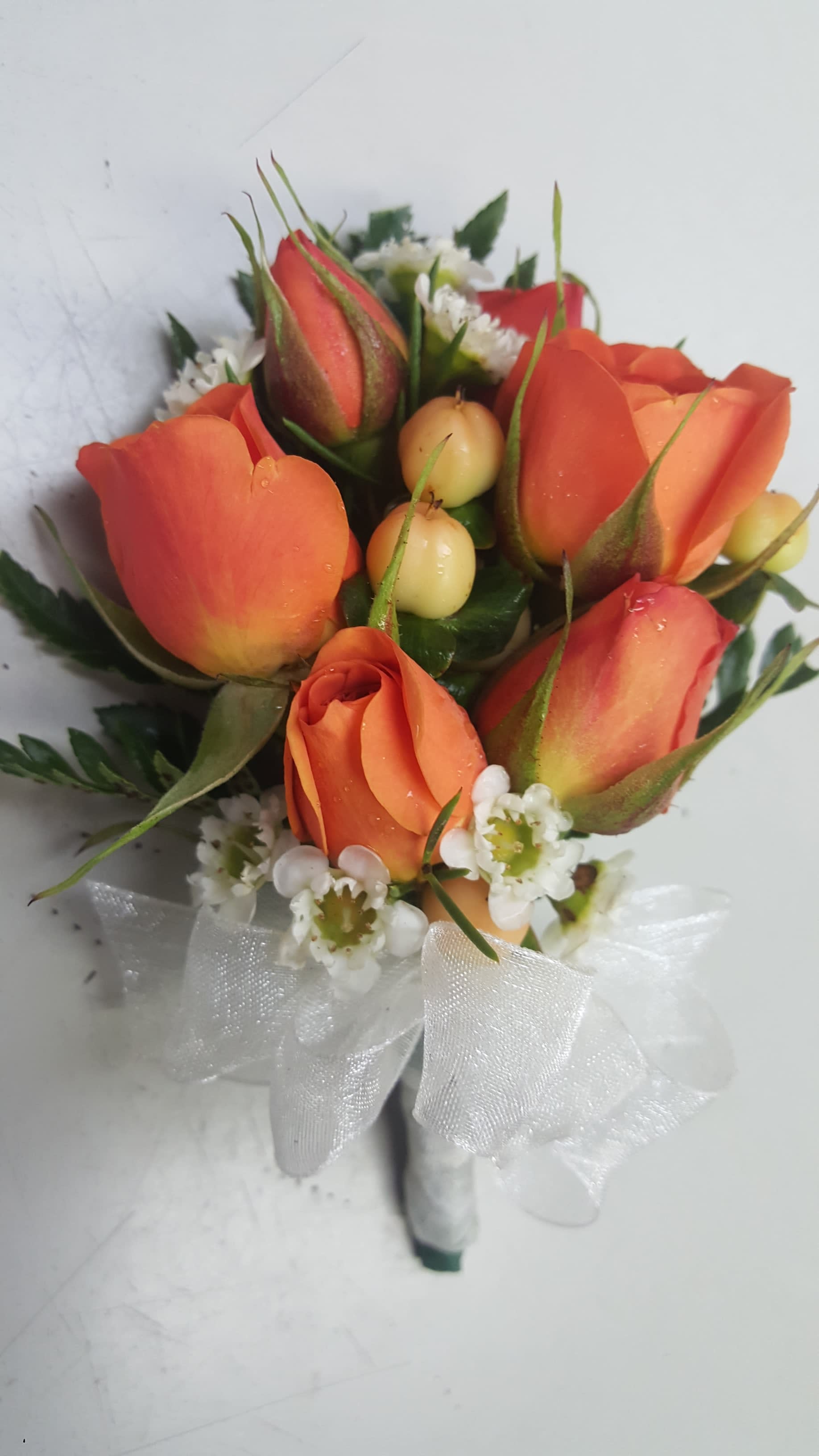 Small bouquet of orange roses with white filler flowers and a white ribbon