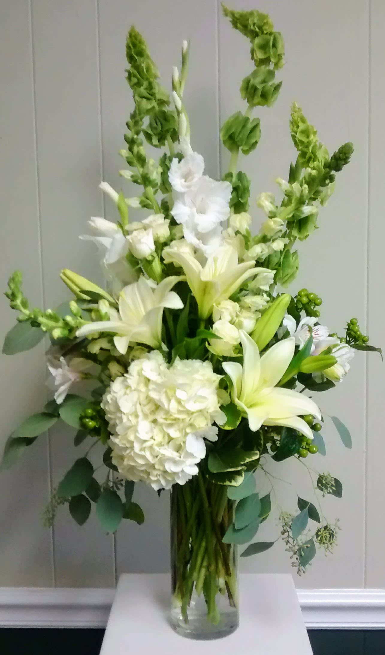 White lilies and hydrangea in a clear glass vase with tall green spikes