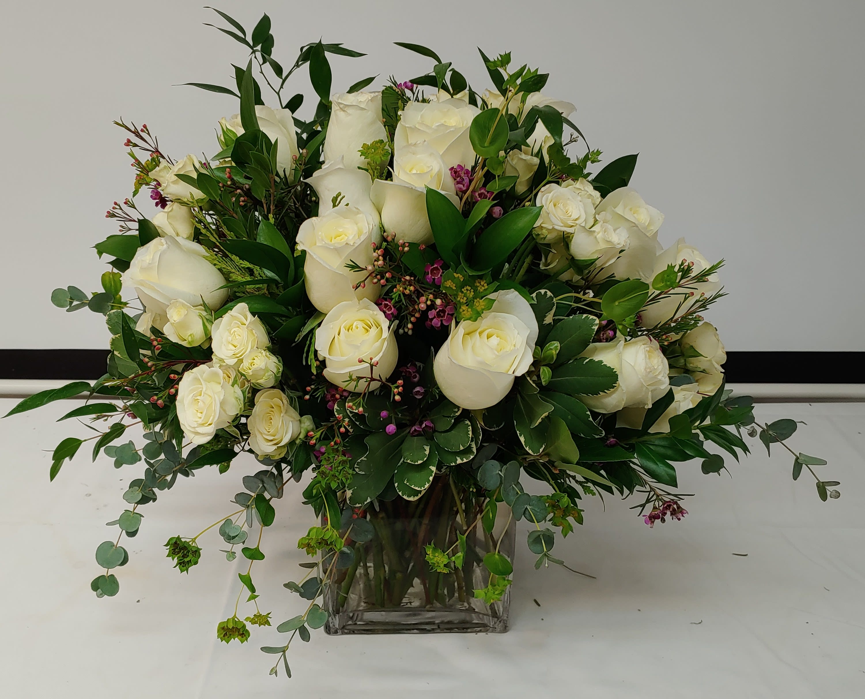 White rose bouquet in a clear glass vase with mixed greenery