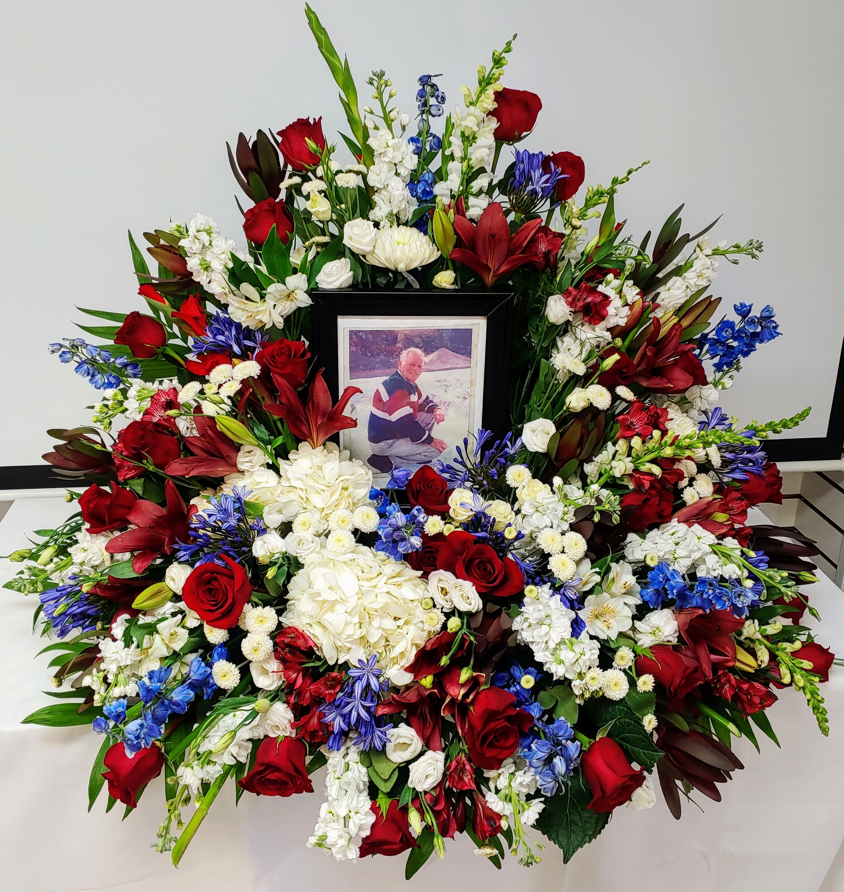 Large funeral wreath of red, white, and blue flowers with a framed photo in the center