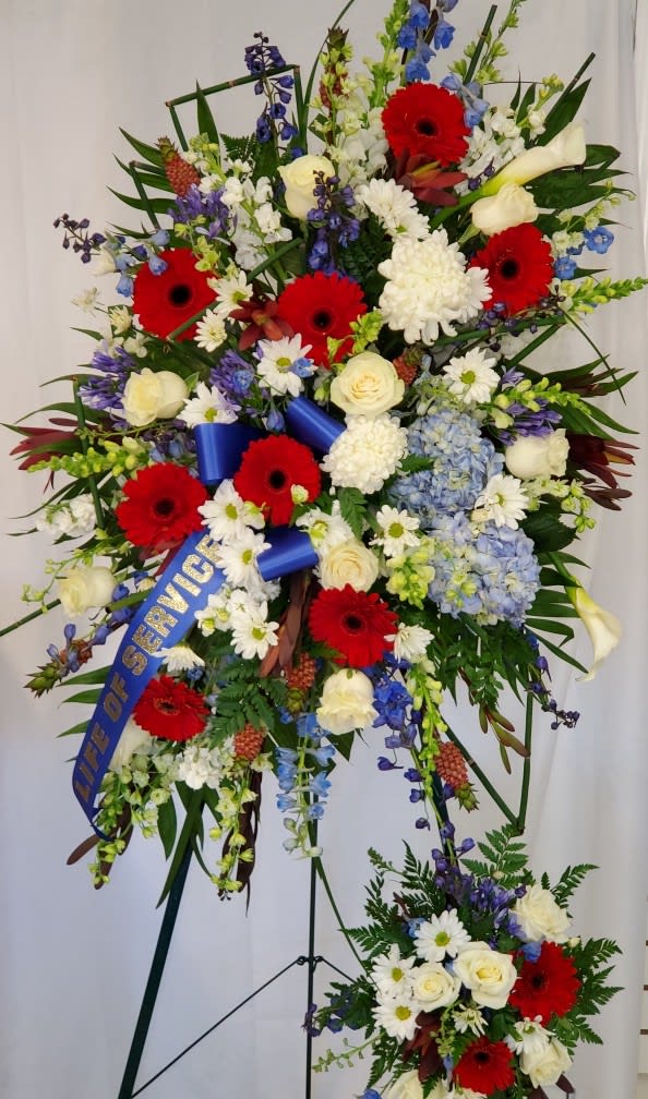 Large standing floral spray with red gerberas, white roses, and blue flowers