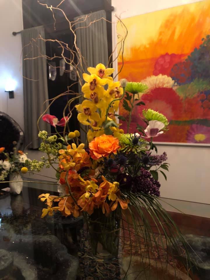 Tall mixed floral arrangement with yellow orchids and orange roses in a glass vase