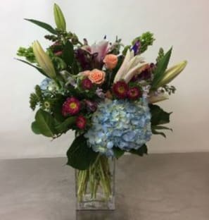 Mixed bouquet with lilies, roses, and blue hydrangea in a clear vase
