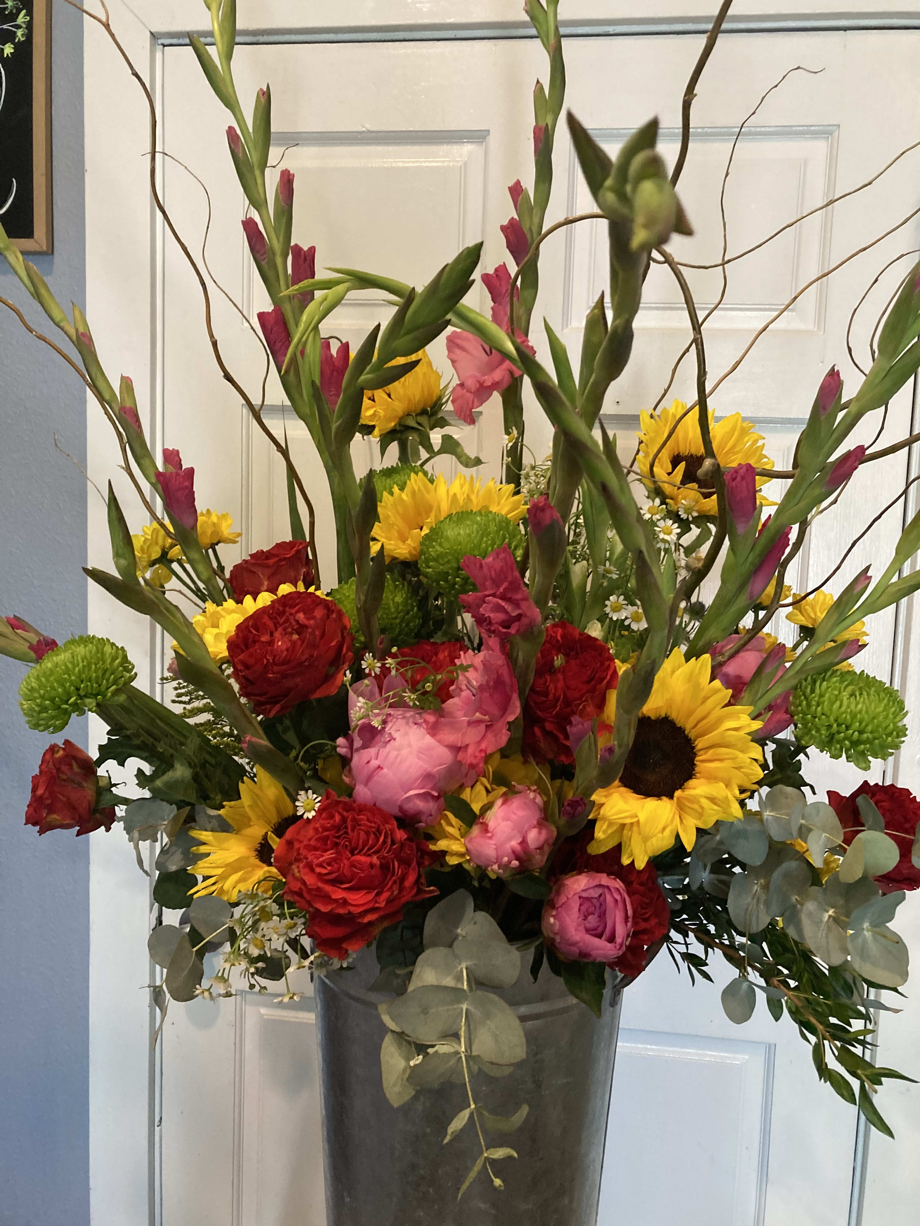 Tall mixed bouquet in a metal vase with sunflowers, red roses, and pink blooms