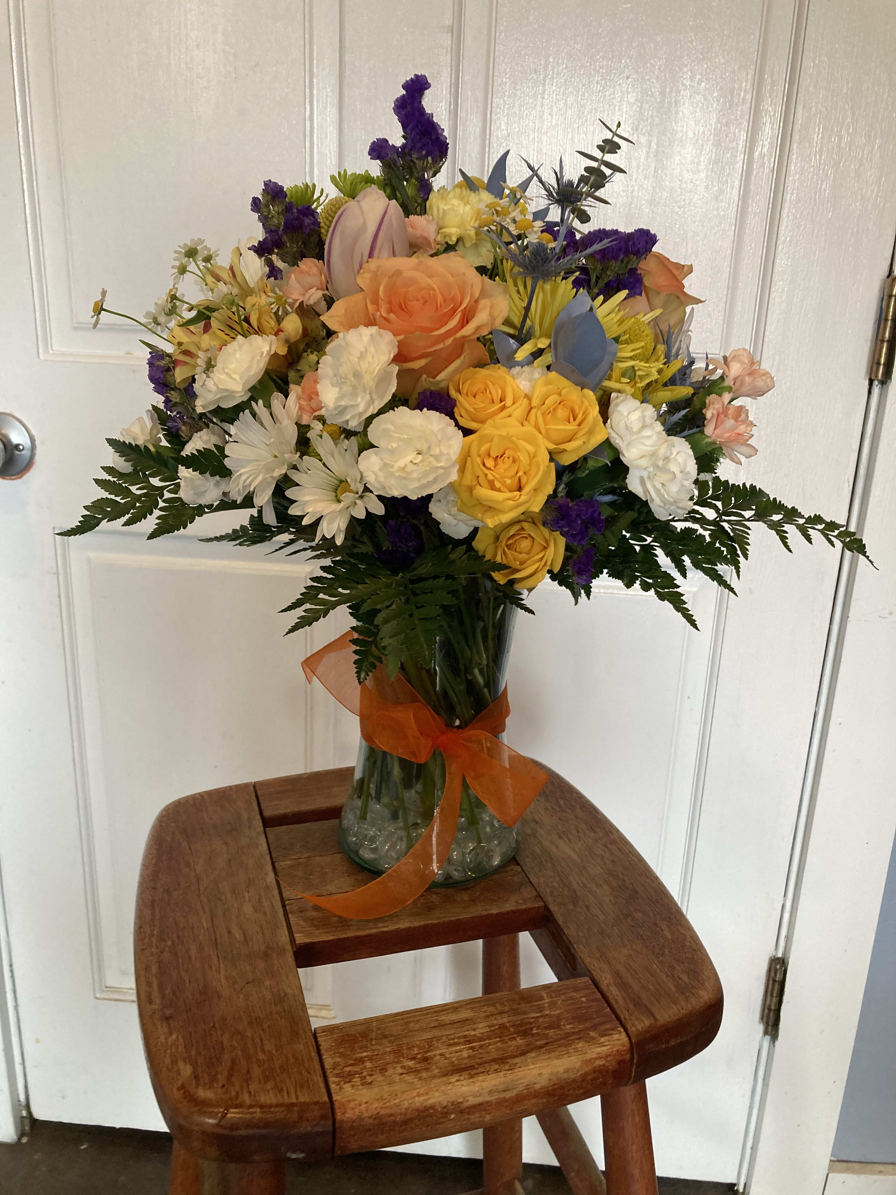 Mixed bouquet of roses, daisies, and purple filler flowers in a glass vase