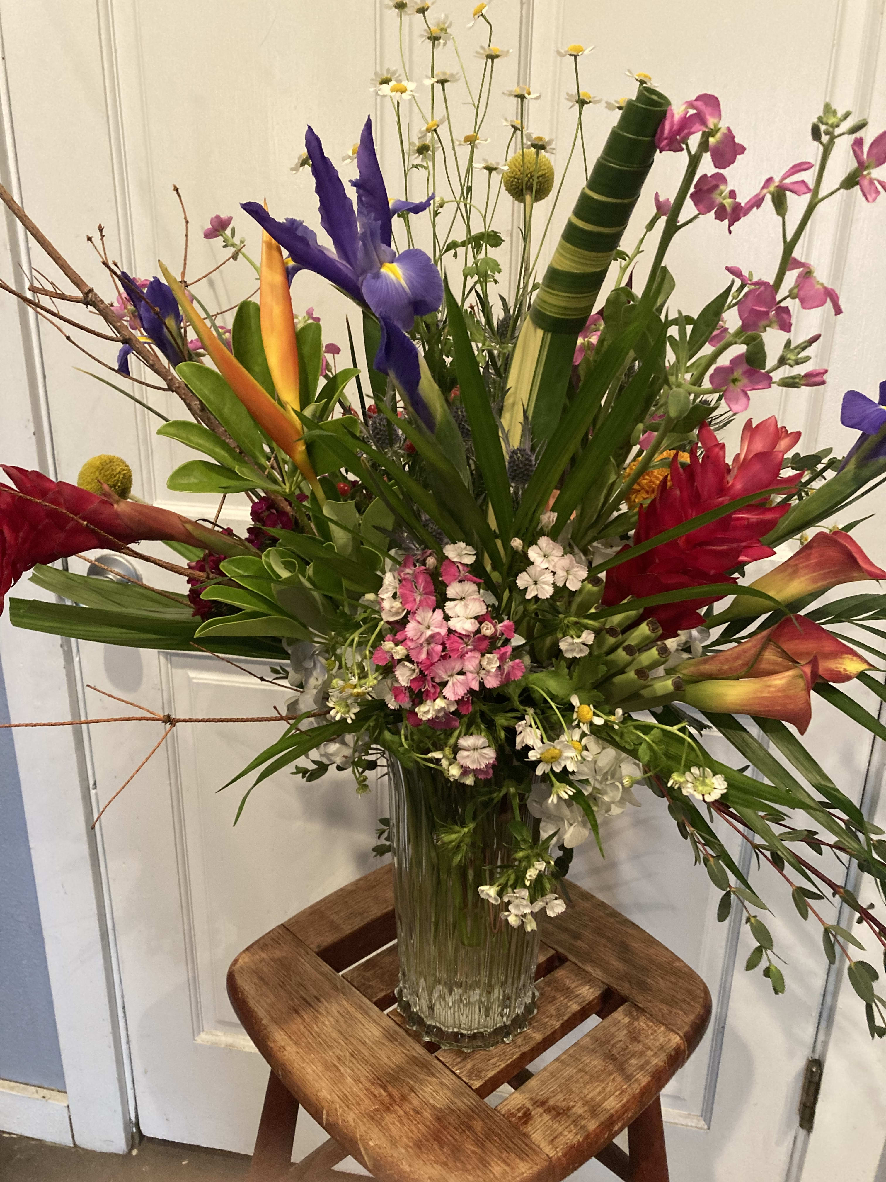 Tropical flower arrangement in a clear glass vase with purple iris and pink blooms