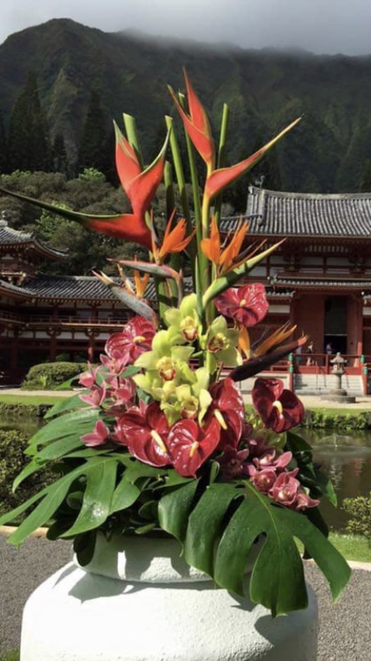 Tropical flower arrangement with orange heliconia and orchids in a white vase