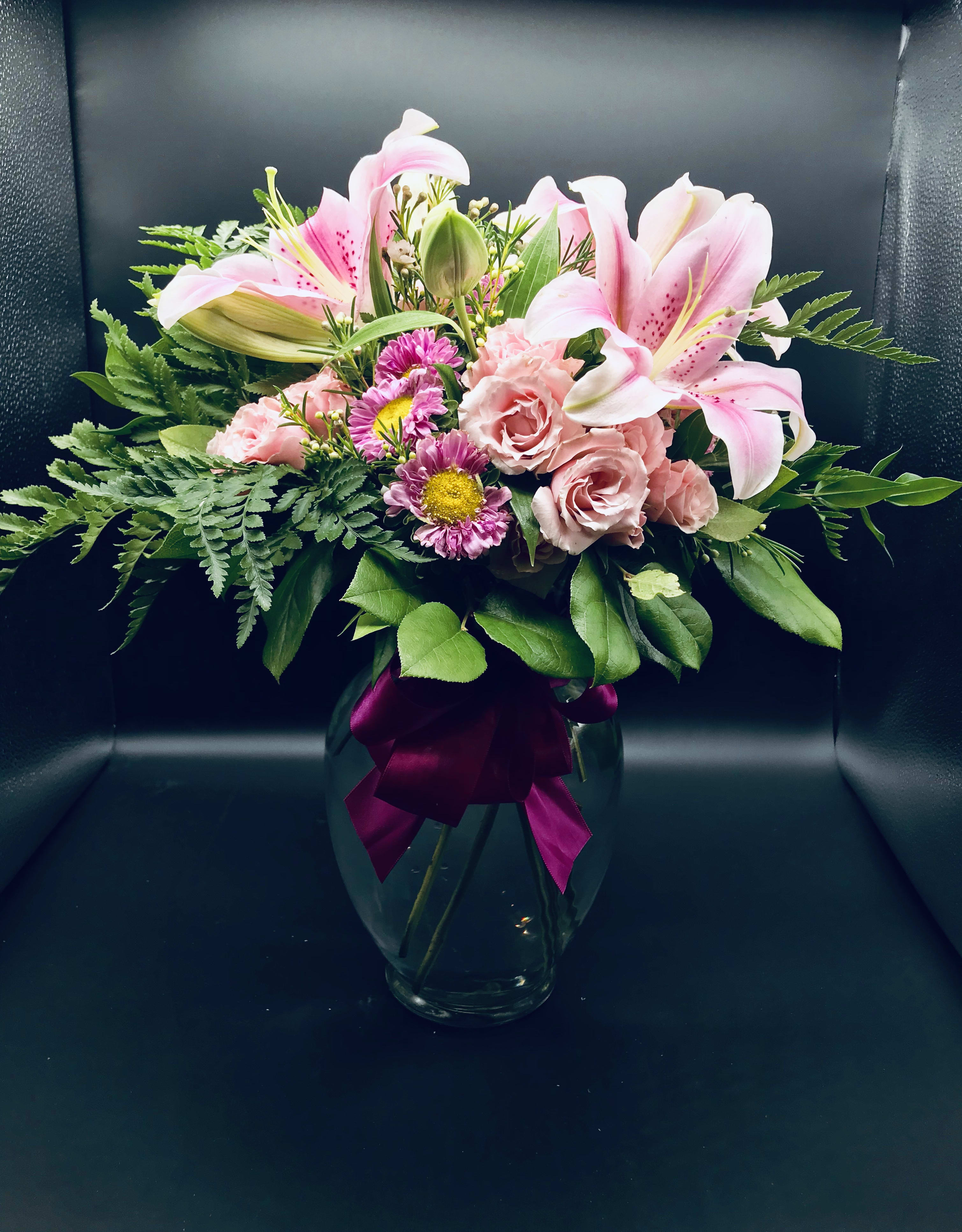 Pink lilies and roses in a glass vase with a magenta ribbon
