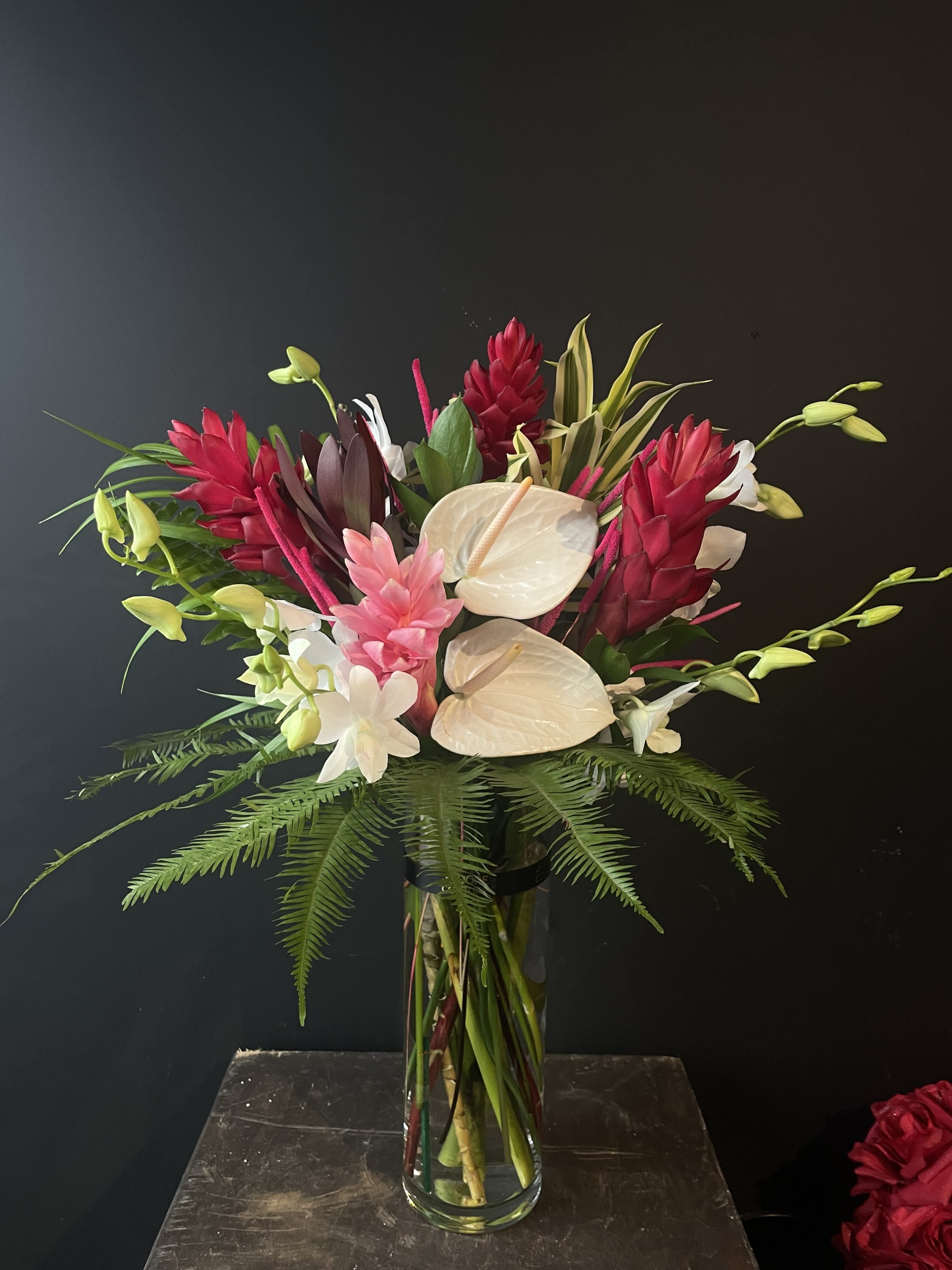 Tropical bouquet with white anthuriums and red ginger in a glass vase